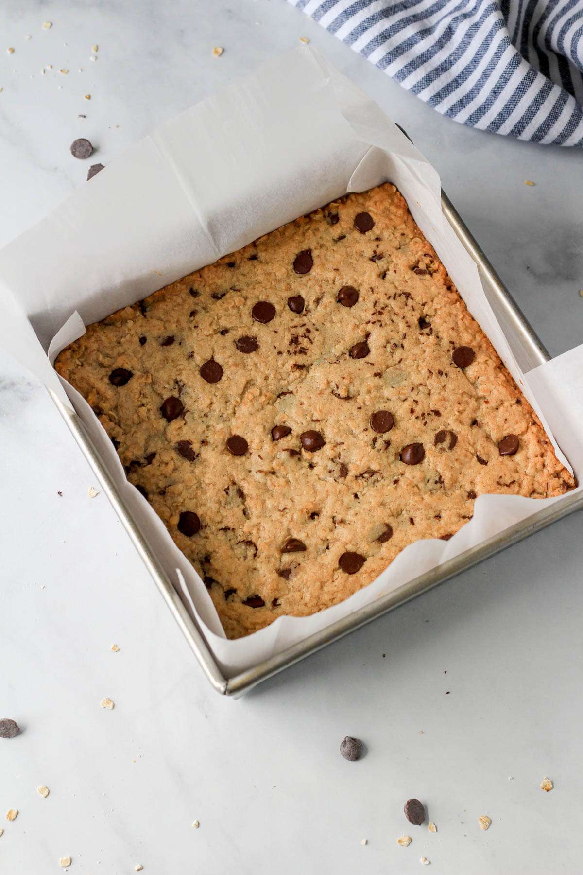 A top down picture of dairy-free oatmeal chocolate chip cookie bars in a metal pan lined with parchment paper.