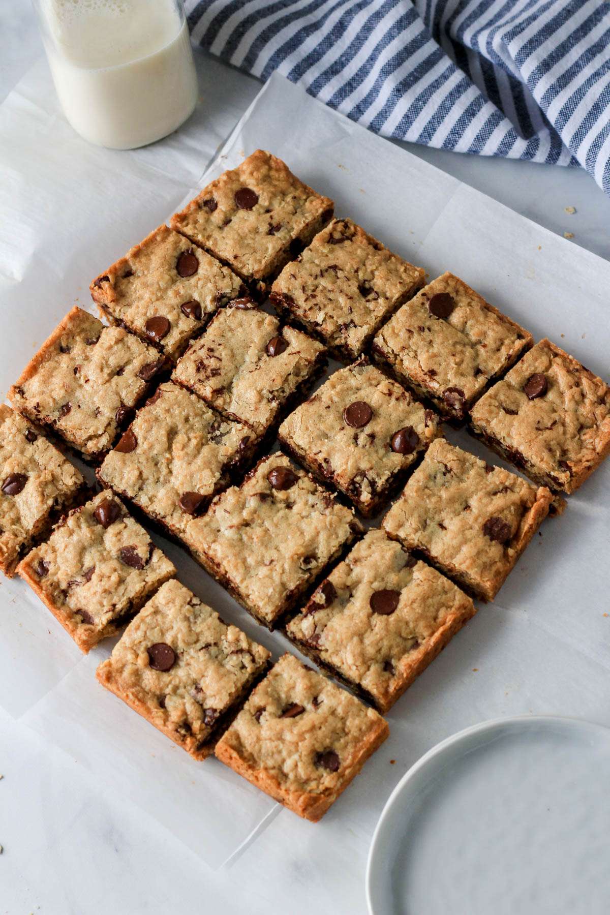 Oatmeal chocolate chip cookie bars cut on a parchment paper with a small glass of non-dairy milk in the back left.