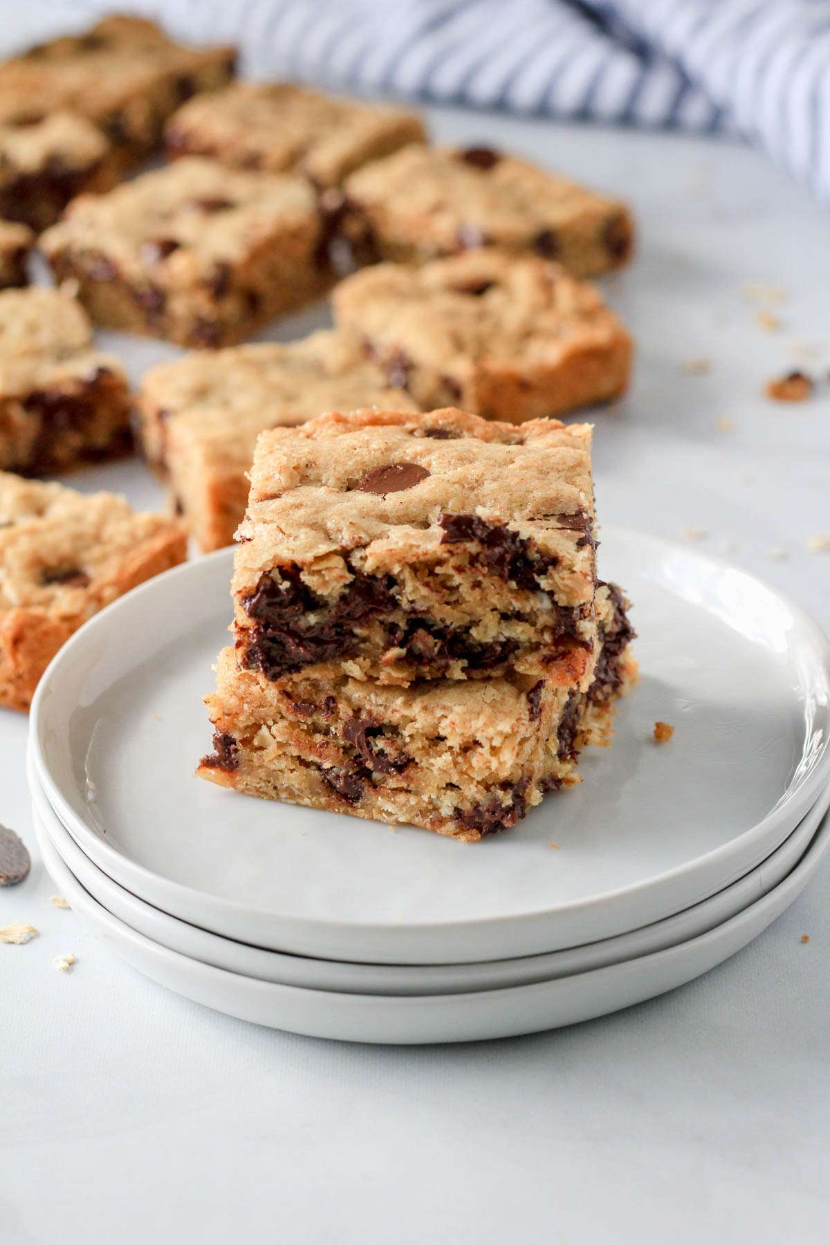 A stack of small white plates topped with two oatmeal chocolate chip cookie bars.
