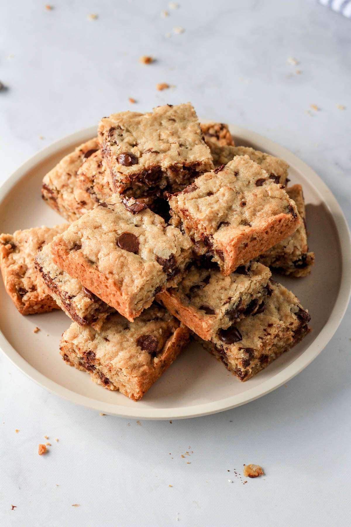 A cream plate on a white counter with a stack of dairy-free oatmeal chocolate chip cookie bars.