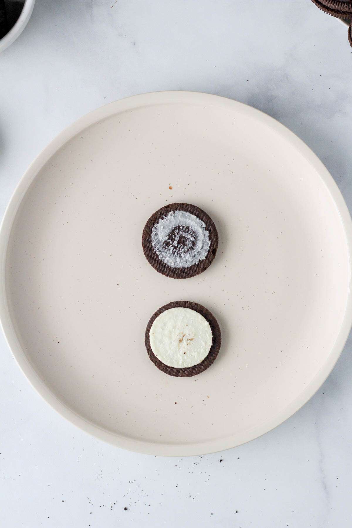 A white plate with an Oreo opened with the creme side on the bottom and the plain side on the top.