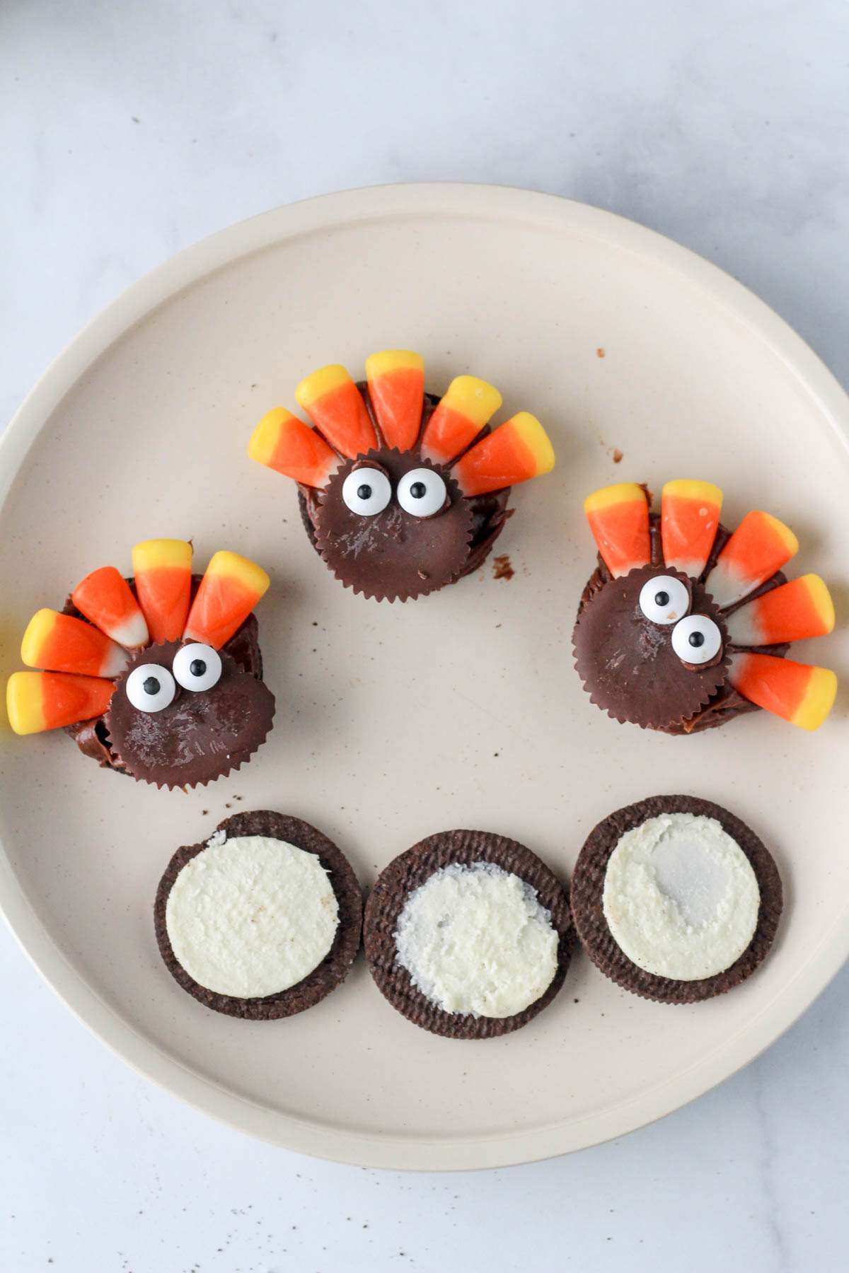 A white plate on a white counter with three Oreo turkey cookies before assembling into an upright shape.