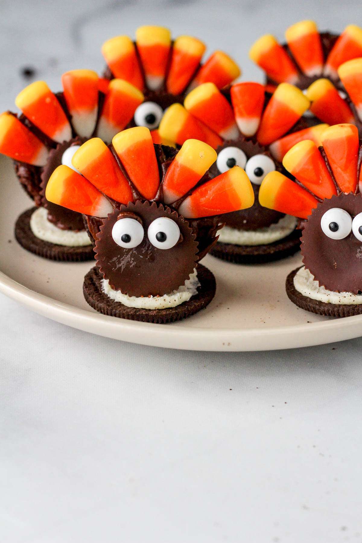 A gaggle of dairy-free Oreo turkey cookies on a white plate on a white counter.