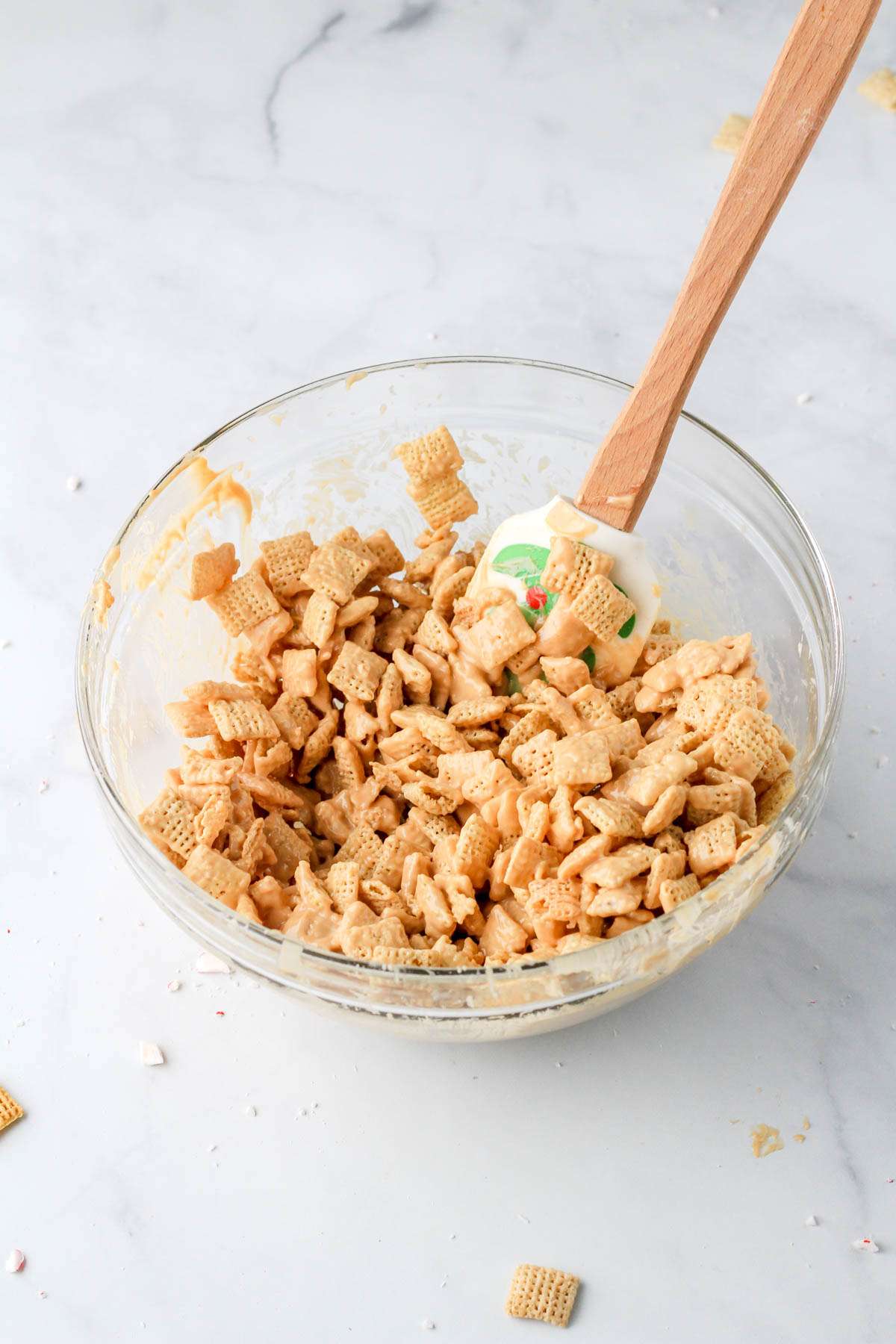 A glass mixing bowl with peppermint white chocolate coated Chex cereal.