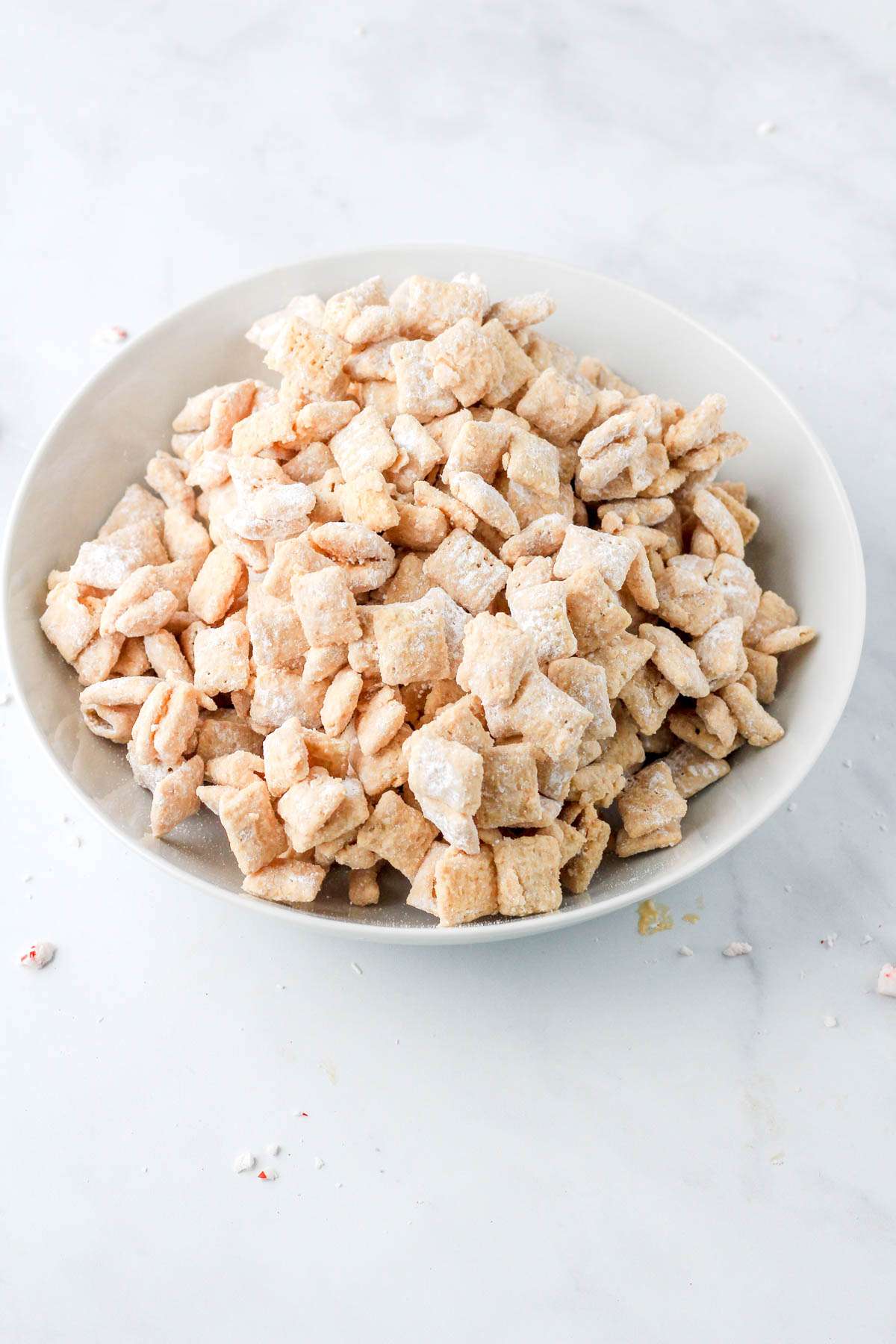 A white bowl with powder sugar coated white chocolate muddy buddies.