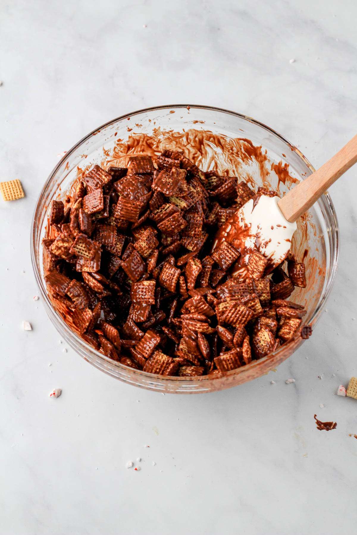A glass mixing bowl with dark chocolate coated Chex cereal before being tossed in powdered sugar.