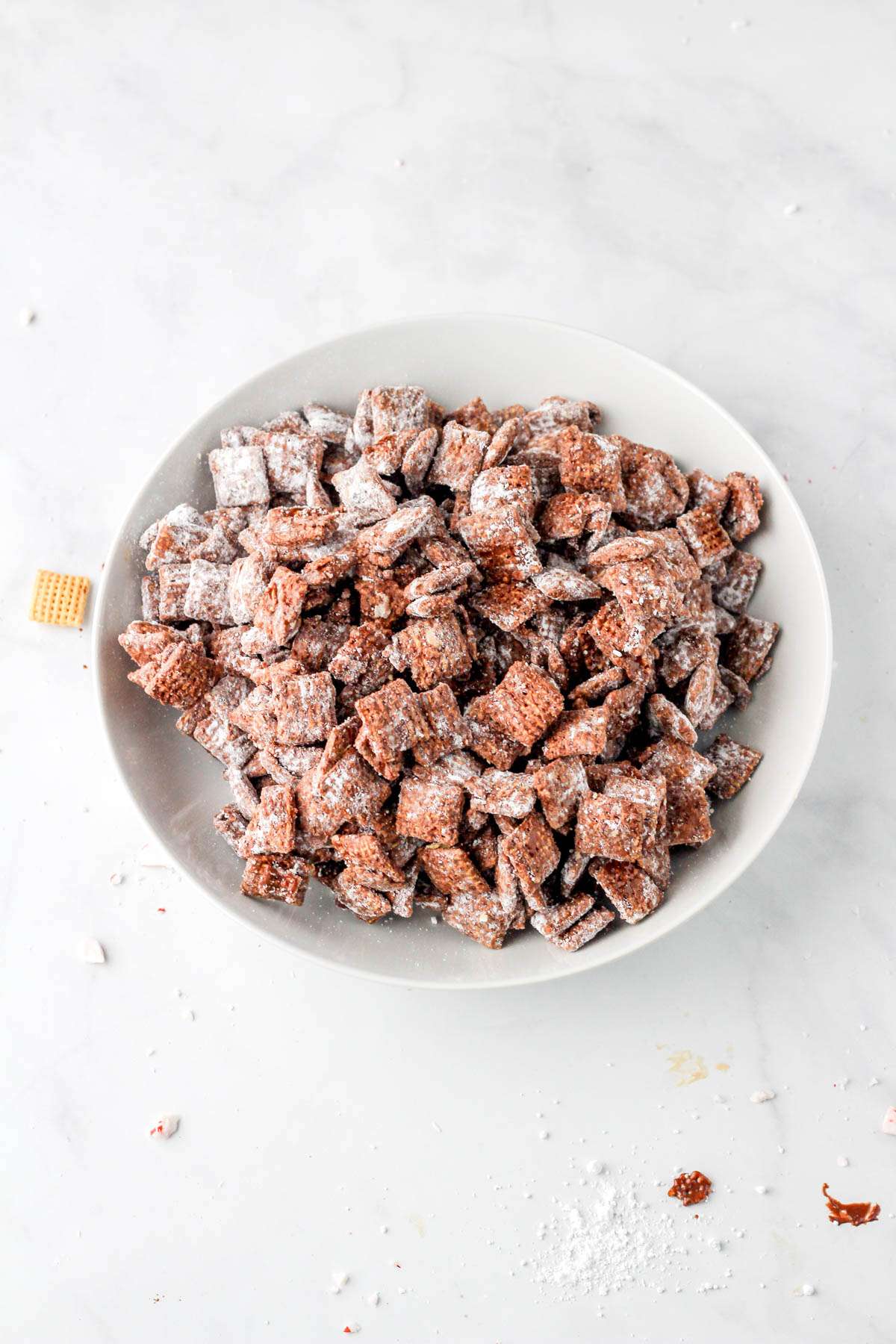 A white bowl with peppermint dark chocolate coated Chex cereal tossed in powdered sugar.