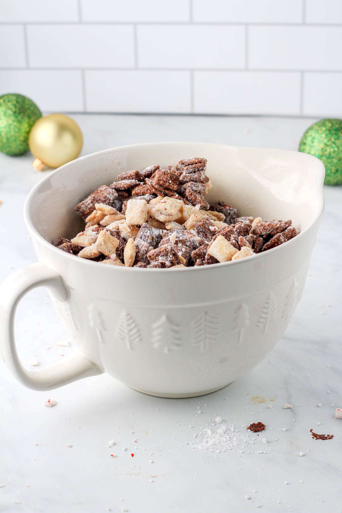 A white mixing bowl with a handle filled with dairy-free peppermint bark puppy chow.