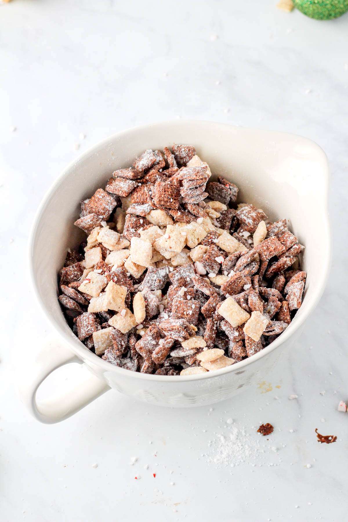 A top down photo of peppermint bark puppy chow in a white mixing bowl with a handle in the bottom left corner.