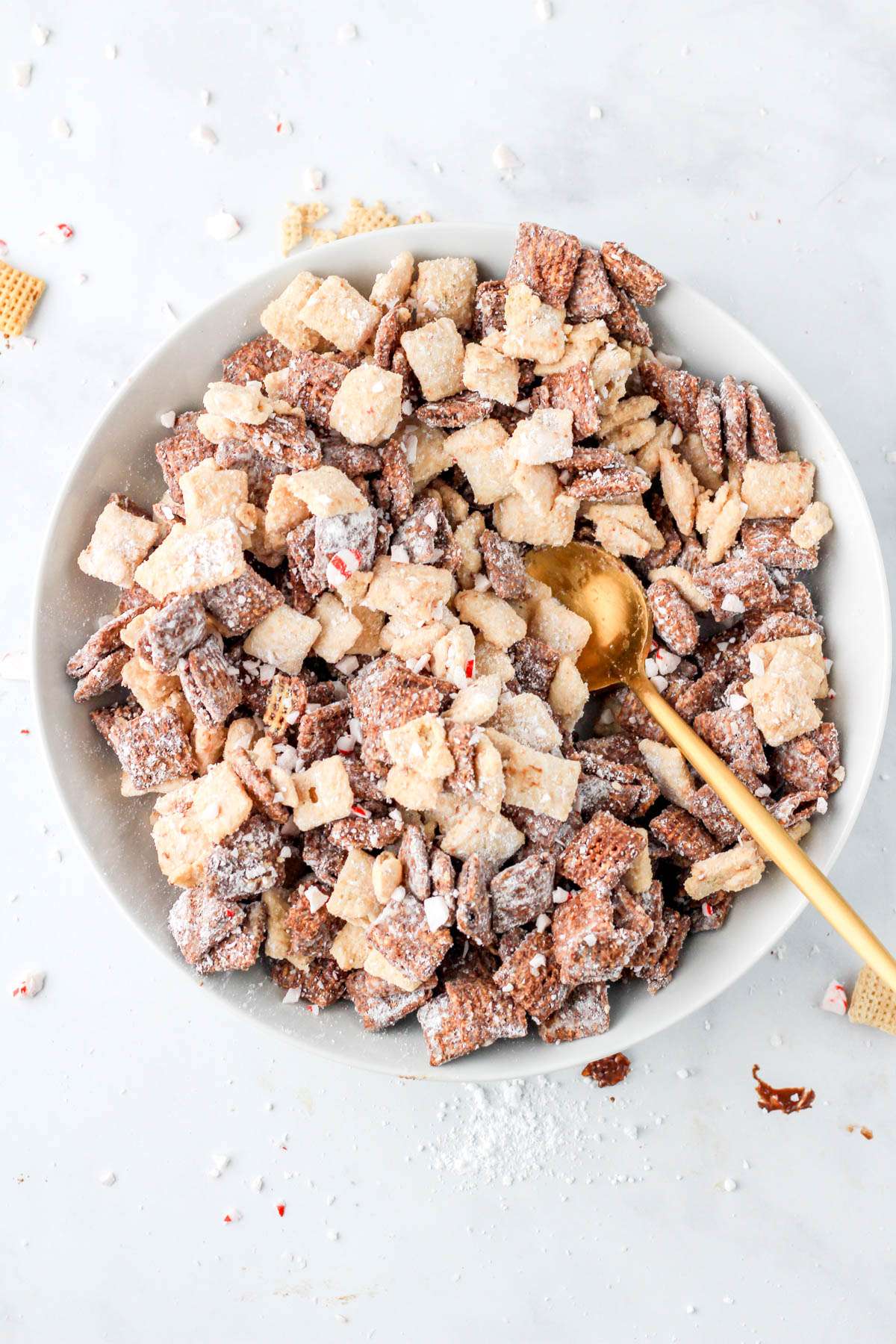 A top down photo of a white bowl filled with dairy-free peppermint bark puppy chow with a gold spoon in the right side of the bowl.