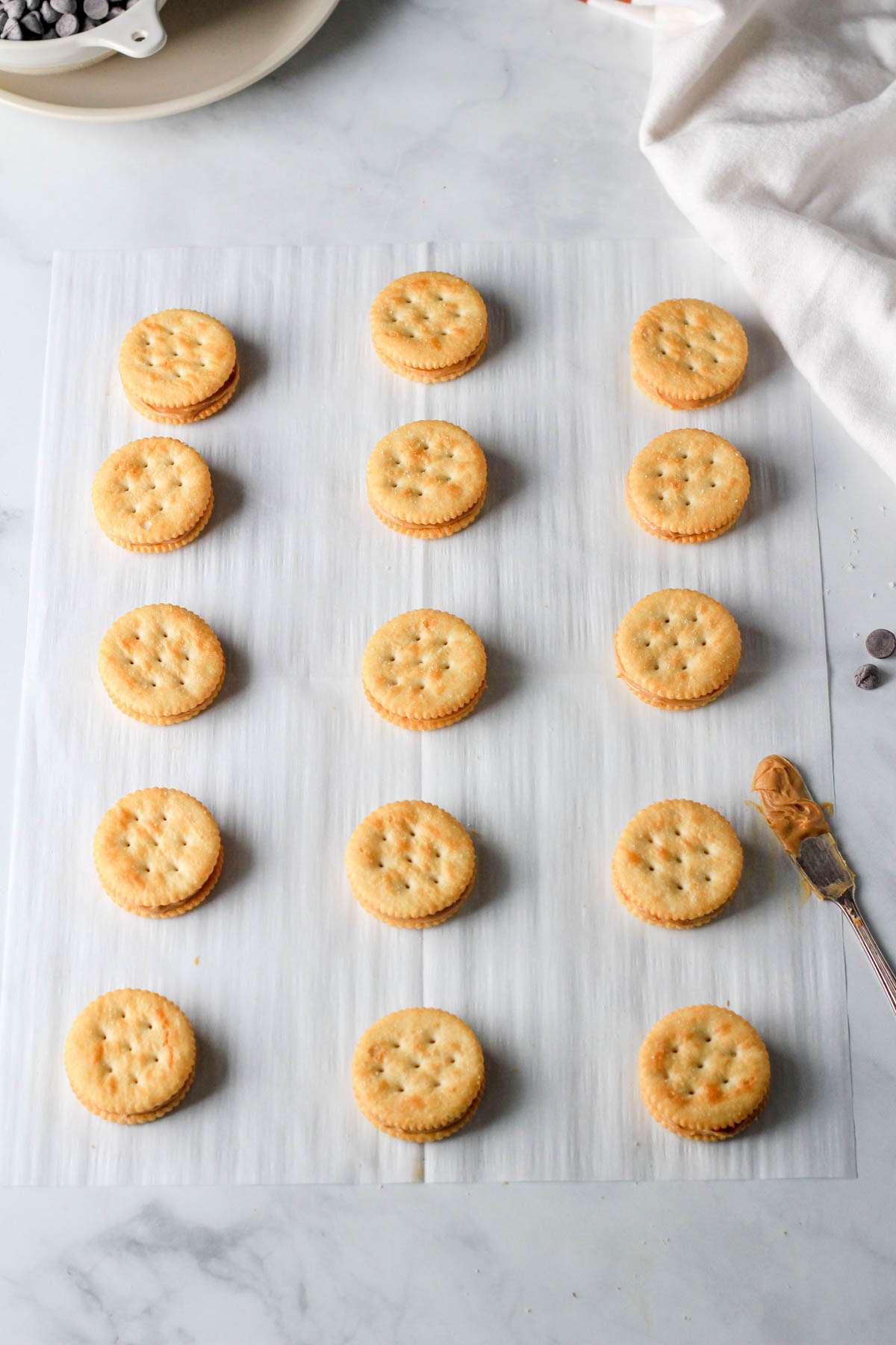 A parchment paper lined with peanut butter Ritz sandwiches before dipping in chocolate.
