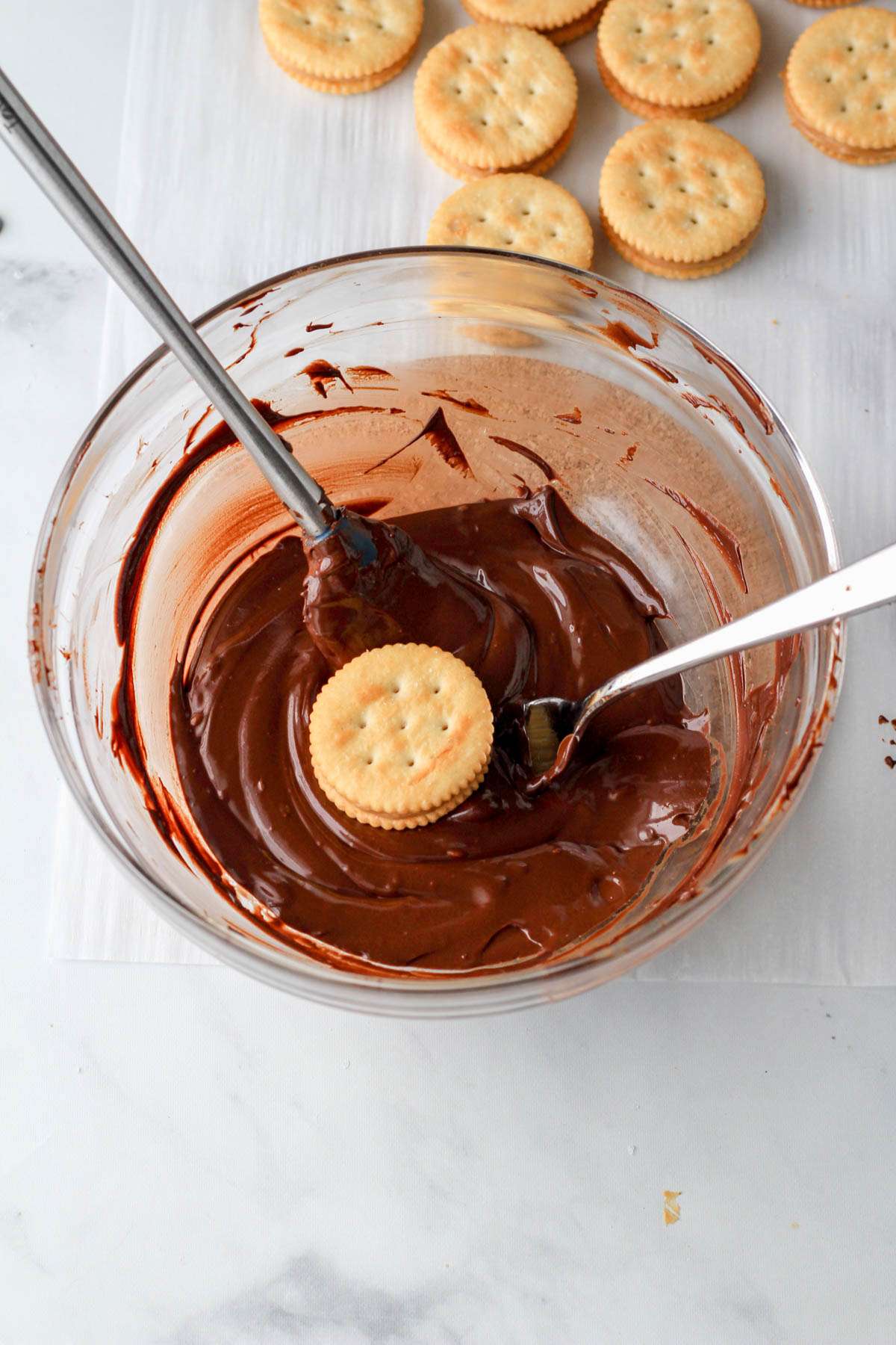 A glass bowl with melted chocolate and a Ritz peanut butter sandwich dipped in the chocolate.