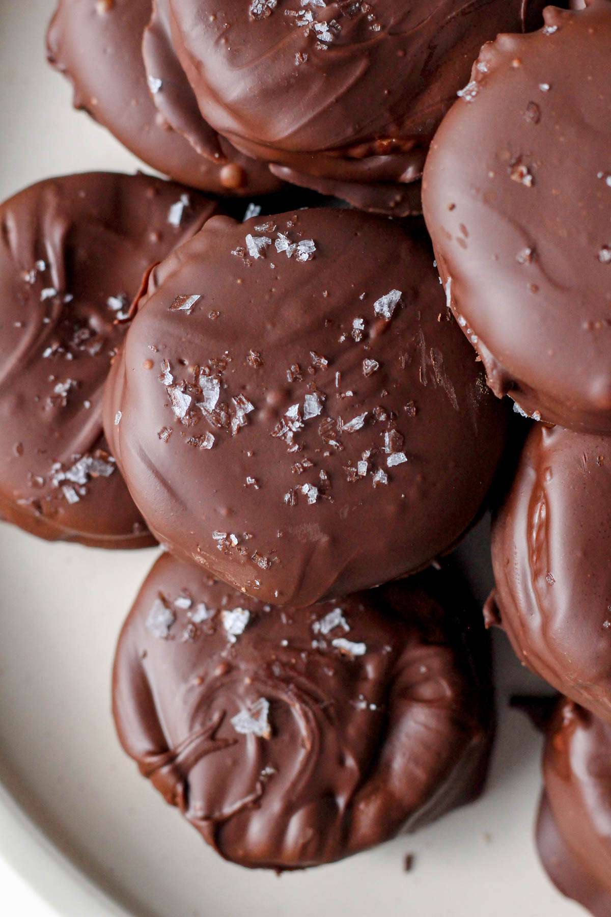 A close up of a pile of vegan chocolate dipped Ritz cookies with flaky sea salt.