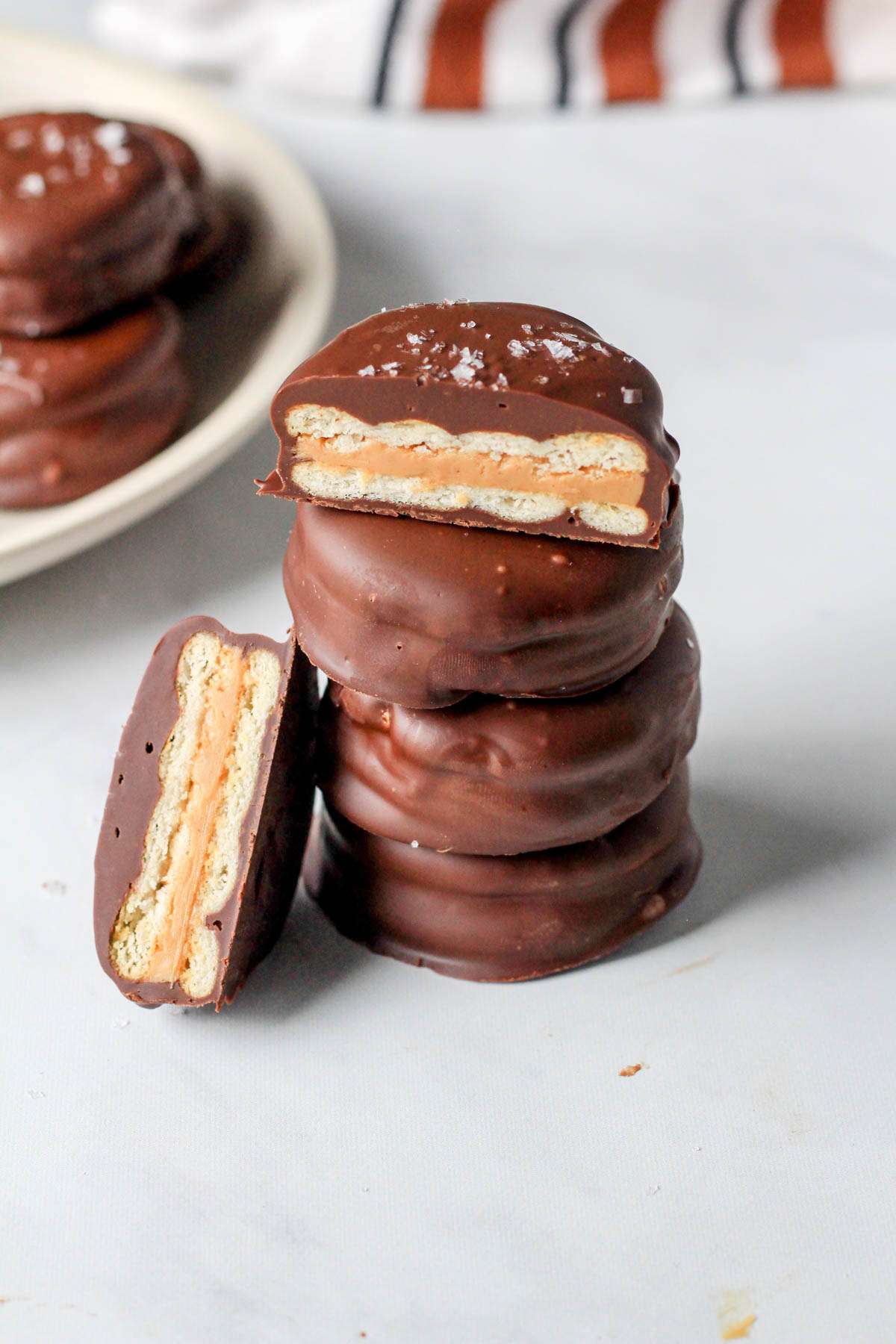 A stack of no-bake chocolate dipped Ritz cookies with one cut on top to show the inside of the vegan cookie.