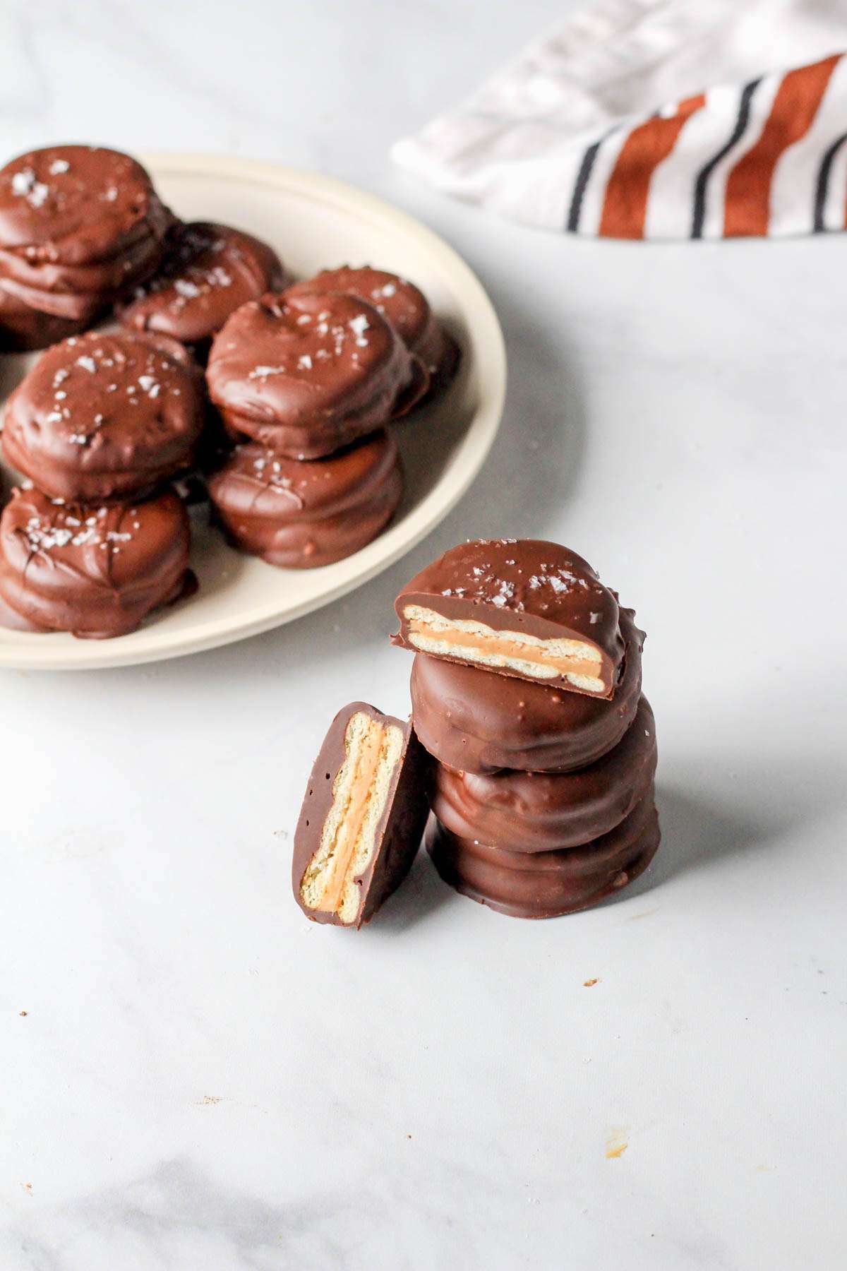 A small pile of chocolate peanut butter Ritz cookies with a white plate of vegan Ritz cookies to the left.