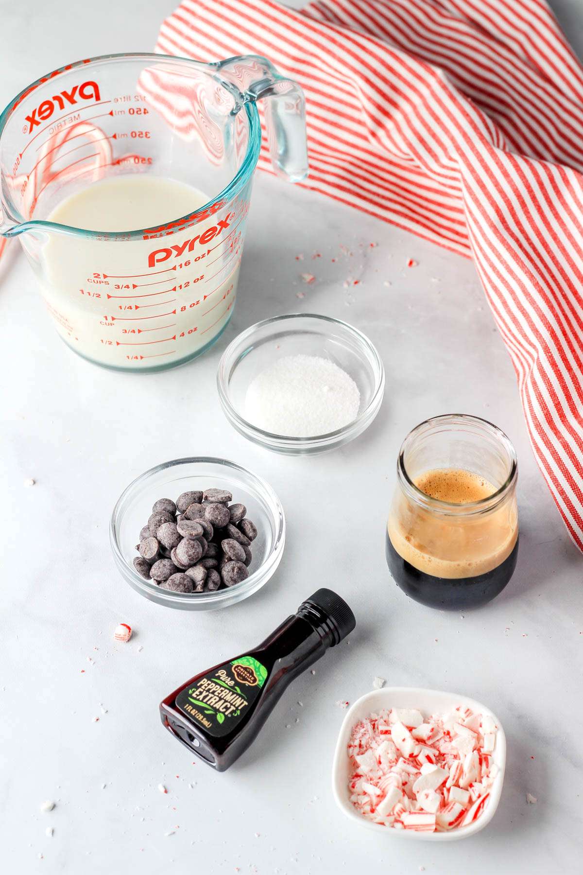 Ingredients for vegan peppermint mocha on a white counter with a red and white striped towel in the back right.