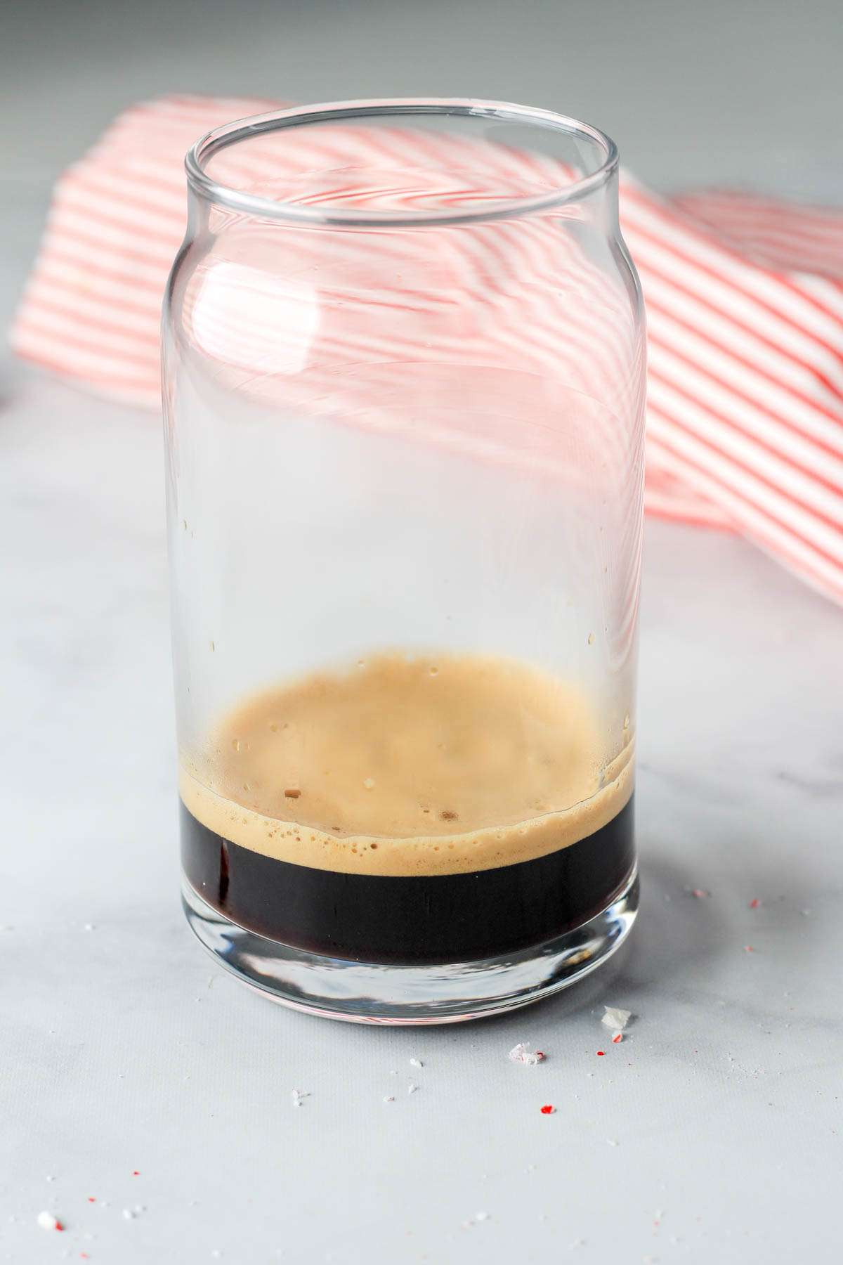 A tall glass cup on a white counter with a double shot of espresso.