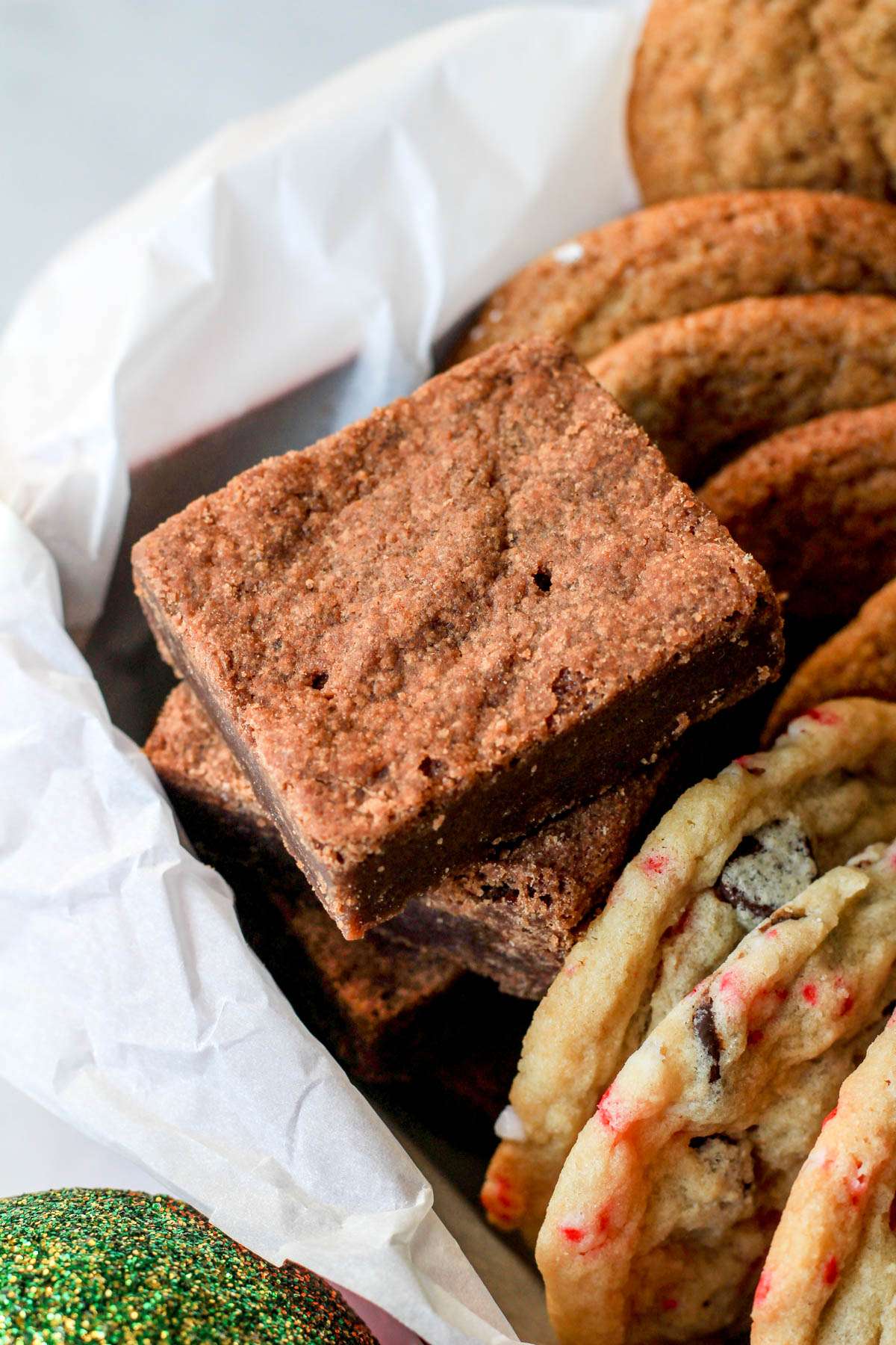 A stack of chocolate shortbread cookies in the back left corner of a red Christmas cookie box.
