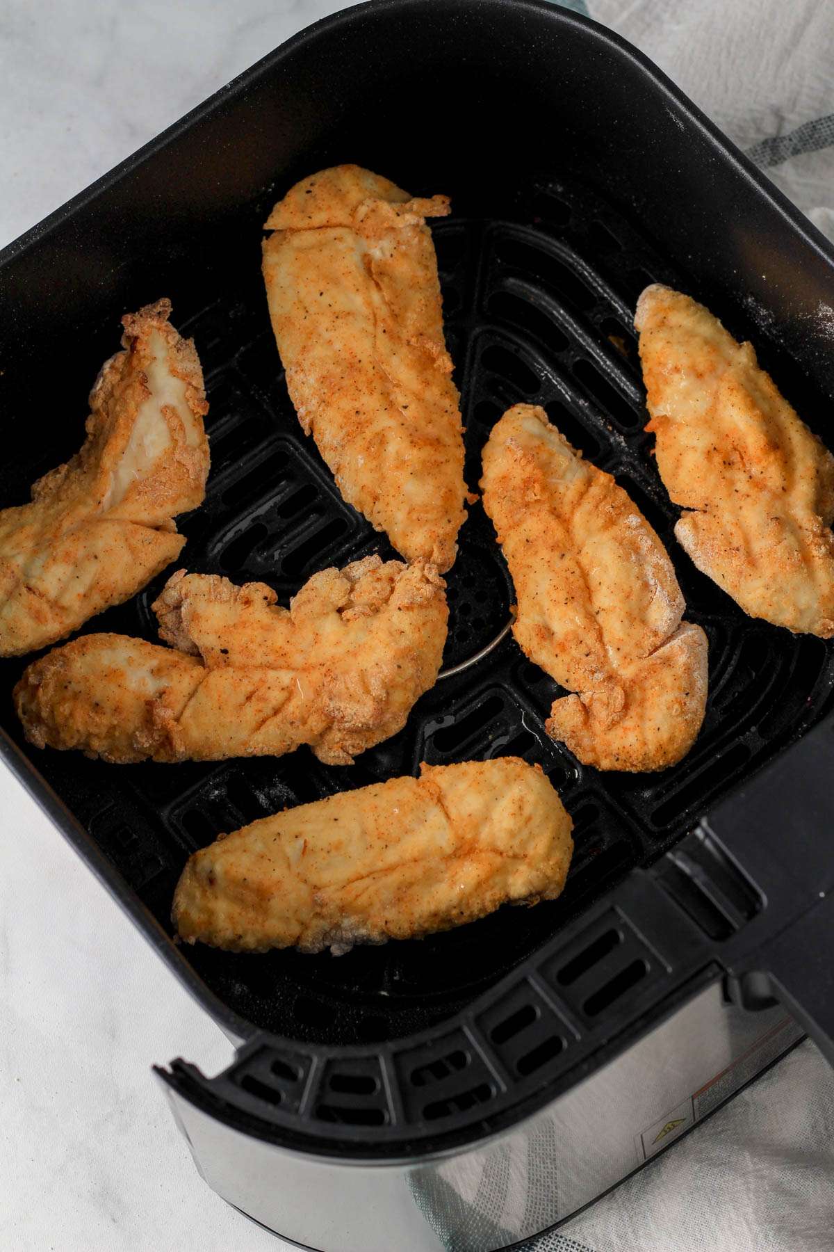 An air-fryer basket with fully cooked chicken tenders.