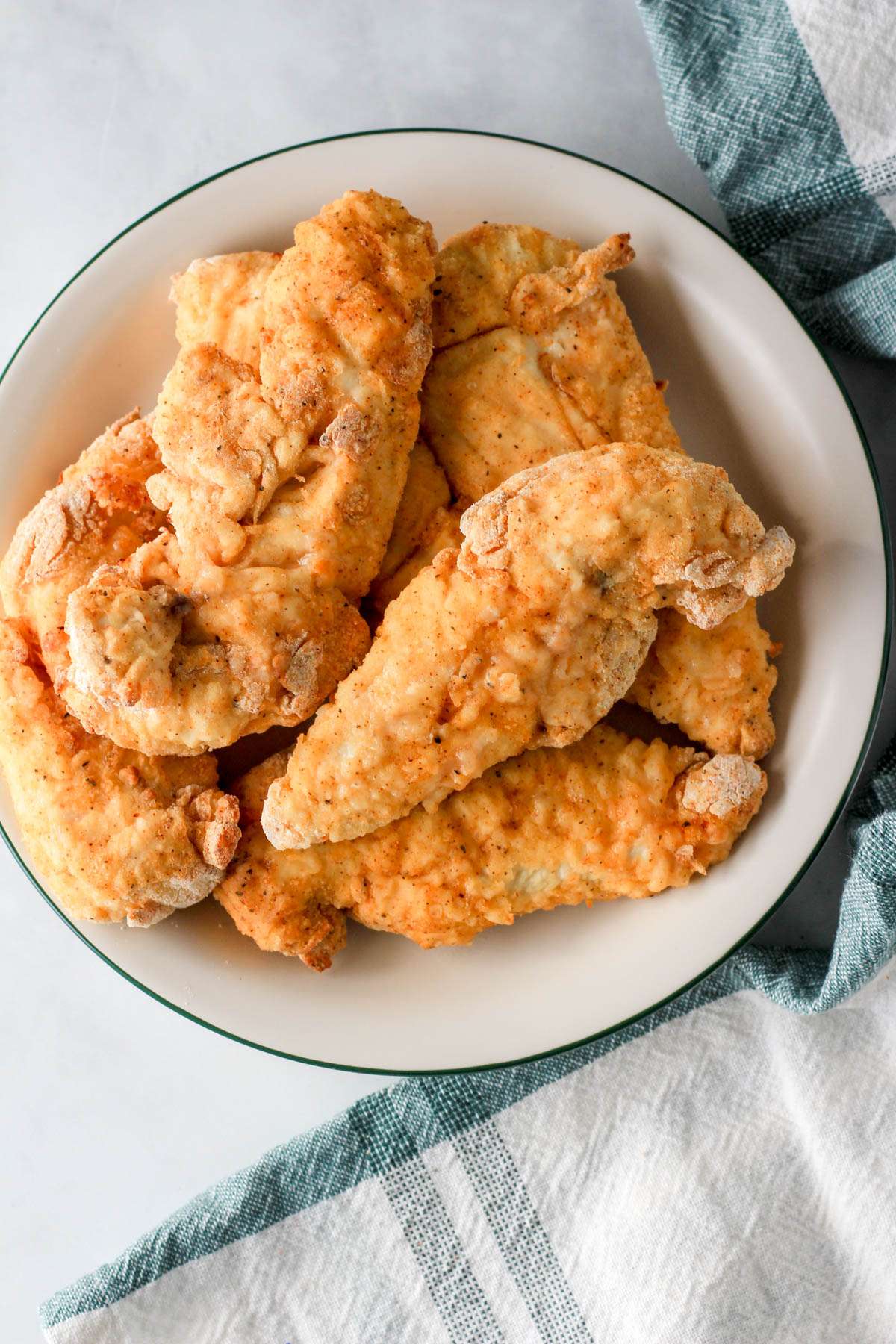 A white plate with a green rim and a pile of air fryer chicken tenders after cooking.