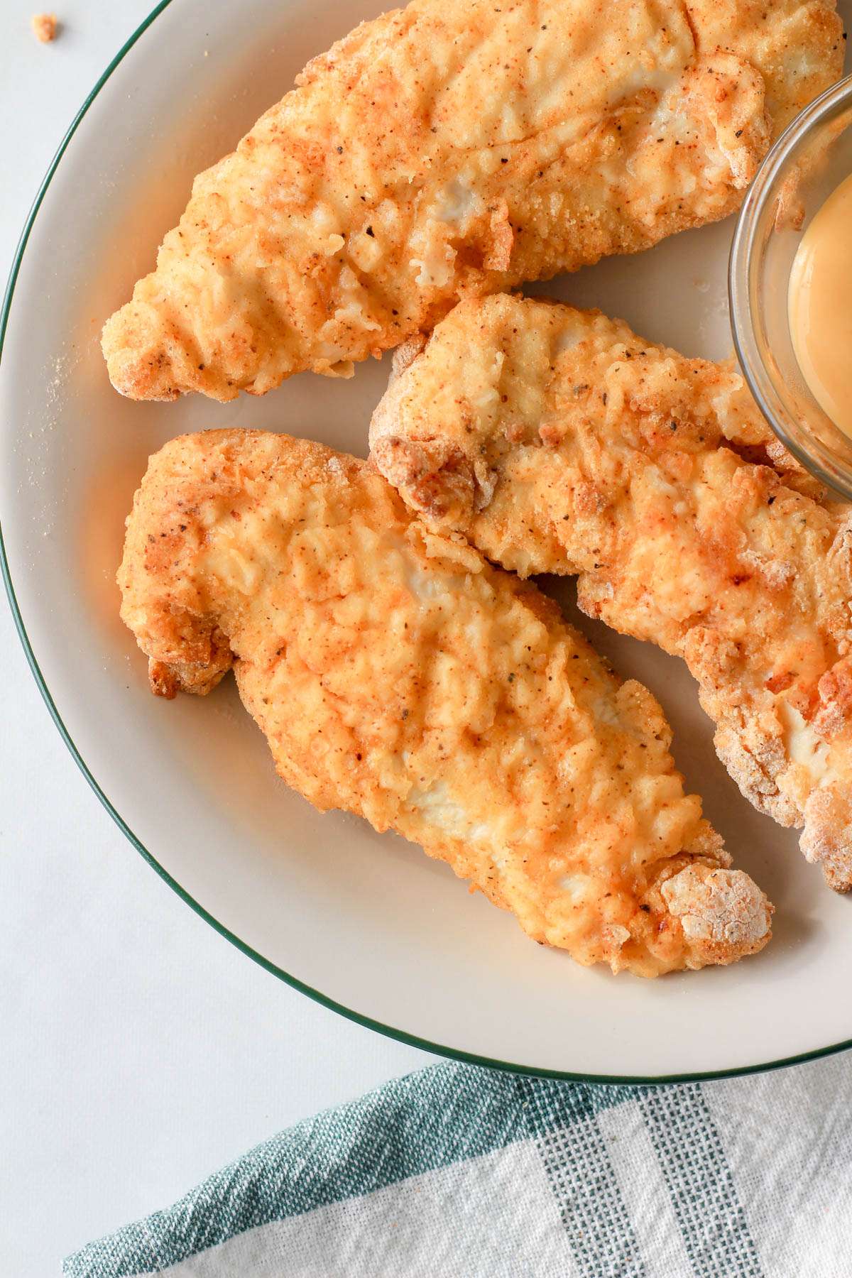 A close up of air fryer chicken tenders on a white and green plate next to a white and green dish towel.