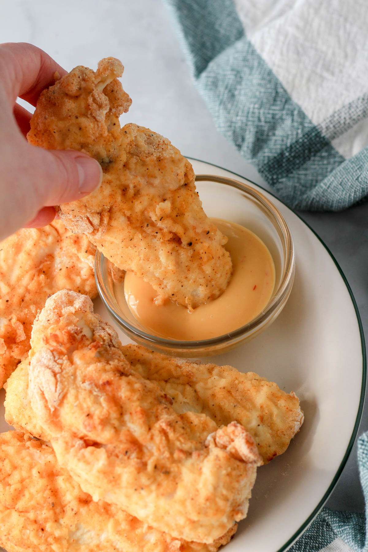 A hand dipping a chicken tender in a small bowl of chick-fil-a sauce.