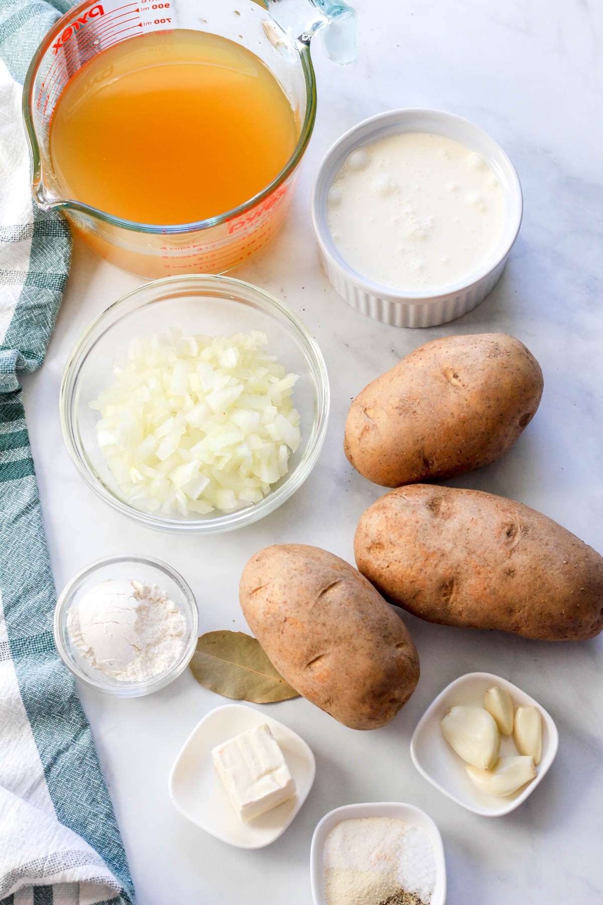Ingredients for dairy-free potato soup on a white counter with a green and white dish towel to the left.