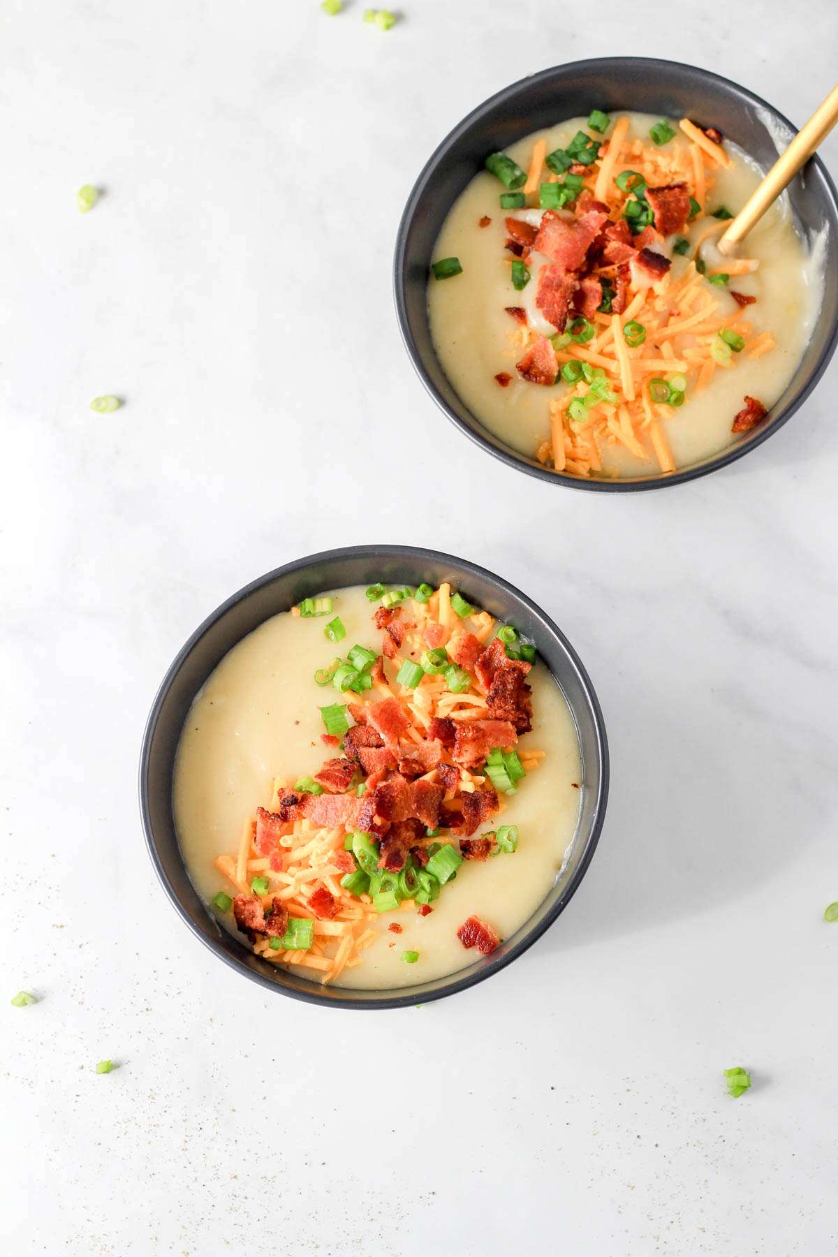 Two bowls of loaded potato soup on a white counter.