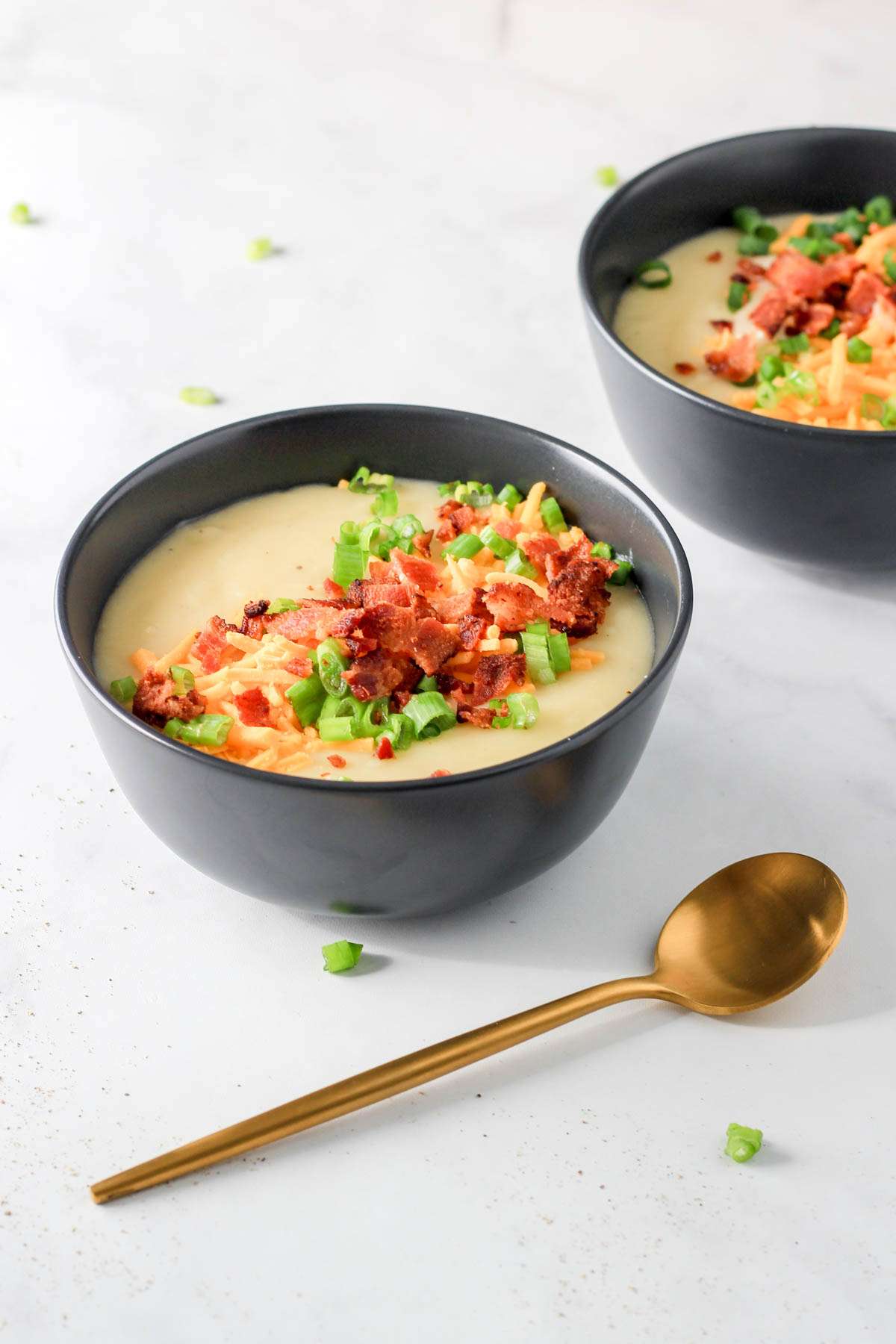 Two bowls of dairy-free potato soup on a white counter with a gold spoon to the right.