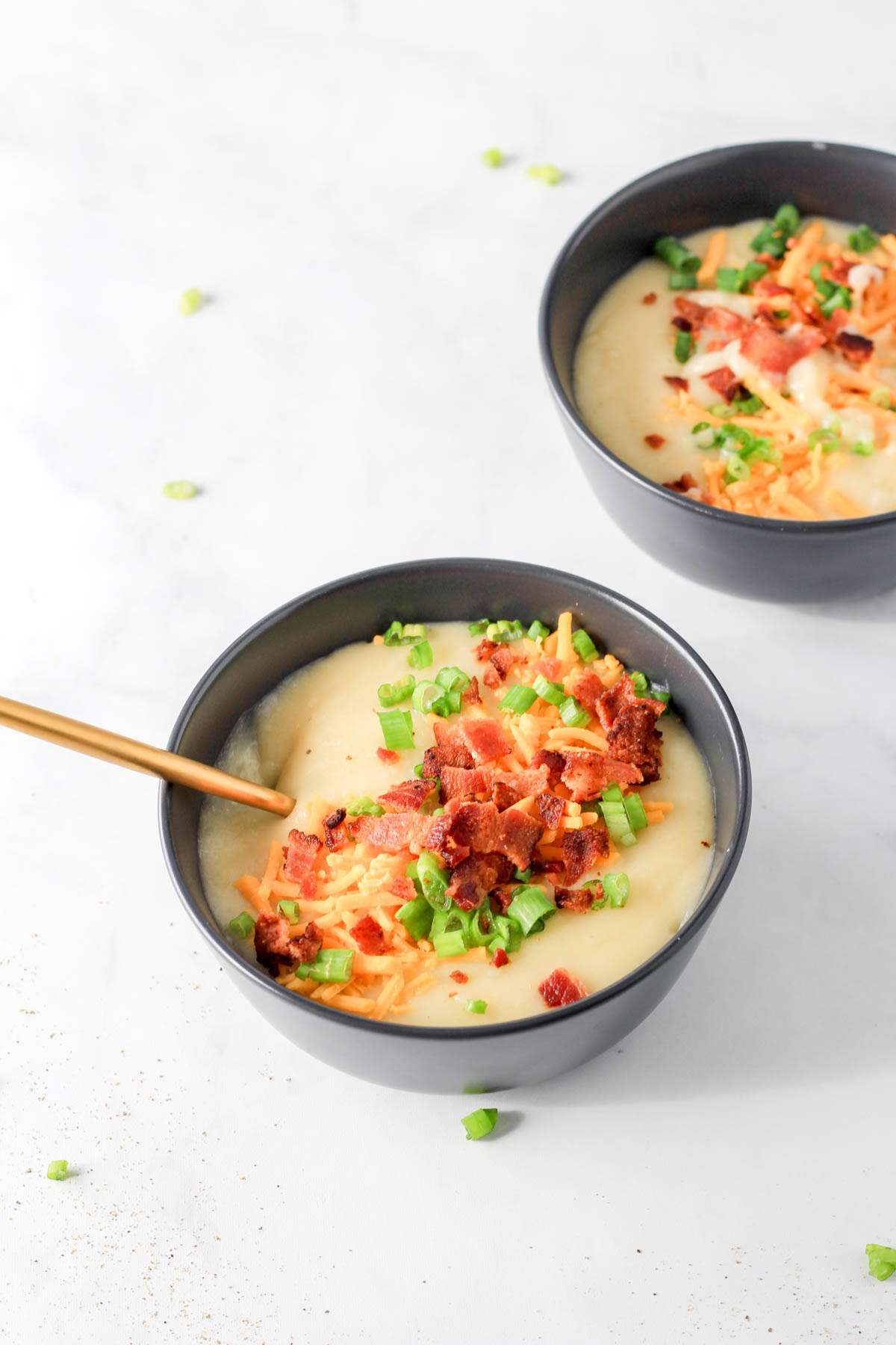 Garnished bowls of dairy-free potato soup on a white counter.