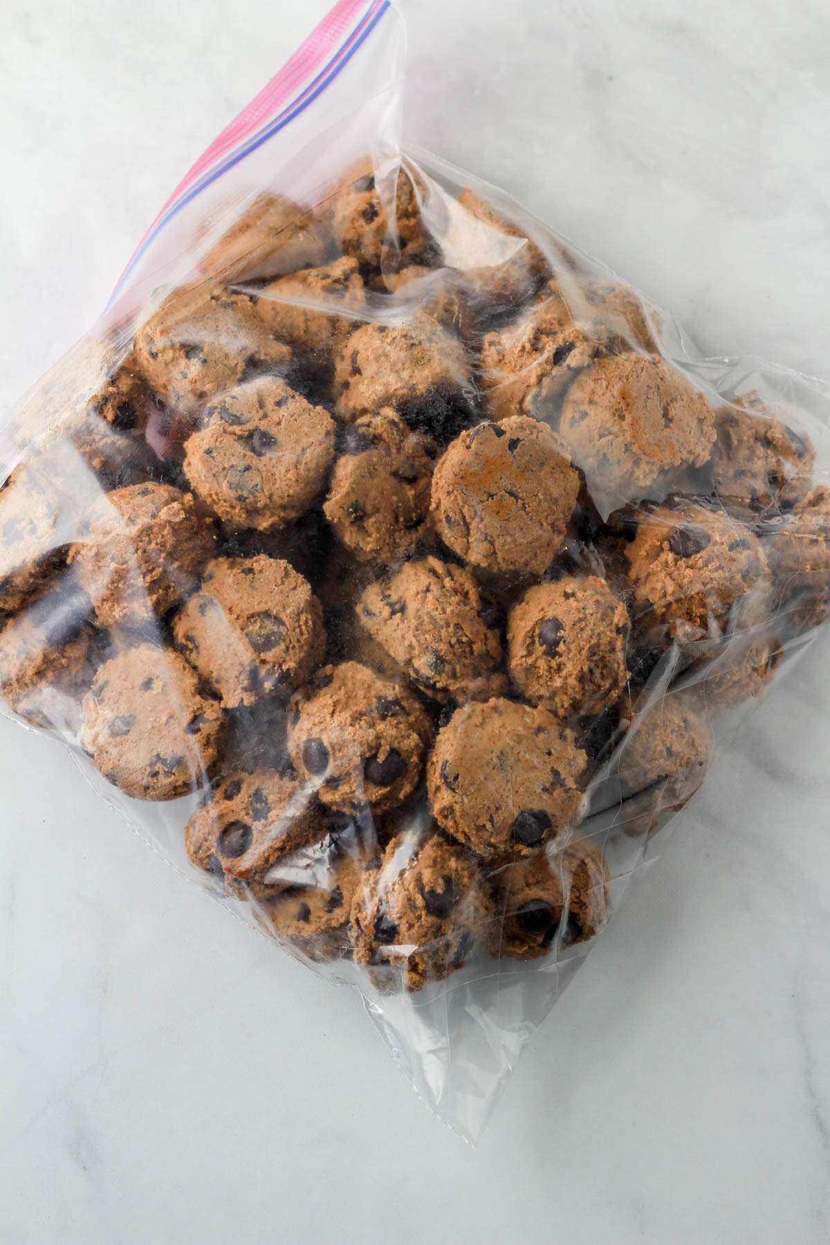 A freezer safe zip top bag with frozen cookie dough balls ready for baking later.