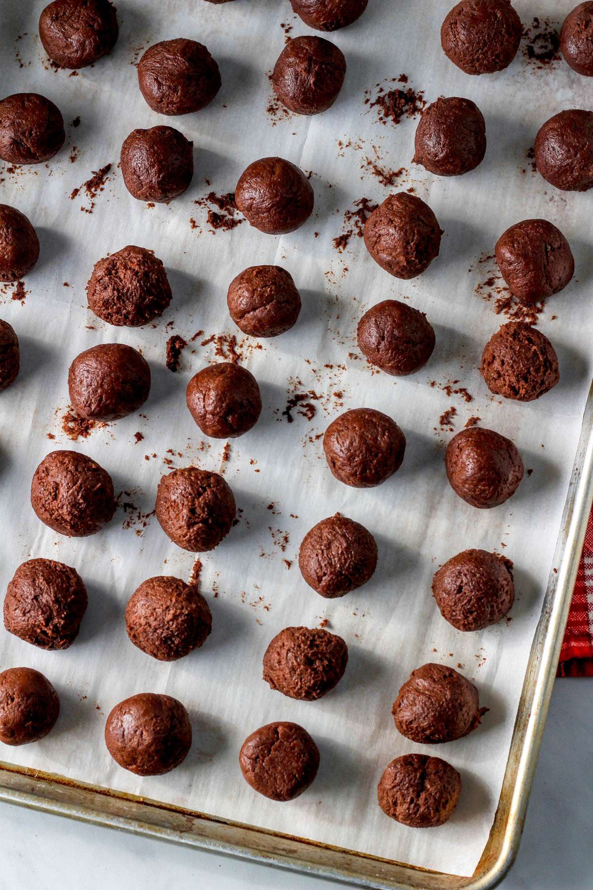 Balls of chocolate crinkle cookie dough on a parchment paper lined baking sheet before going in the freezer.