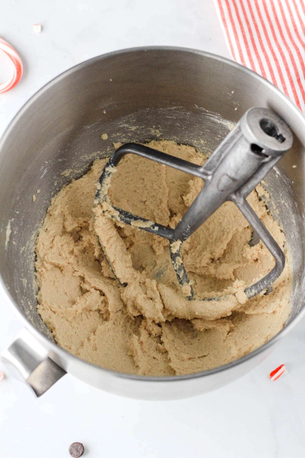 A silver mixing bowl with a paddle attachment and creamed butter and sugars in the bowl.