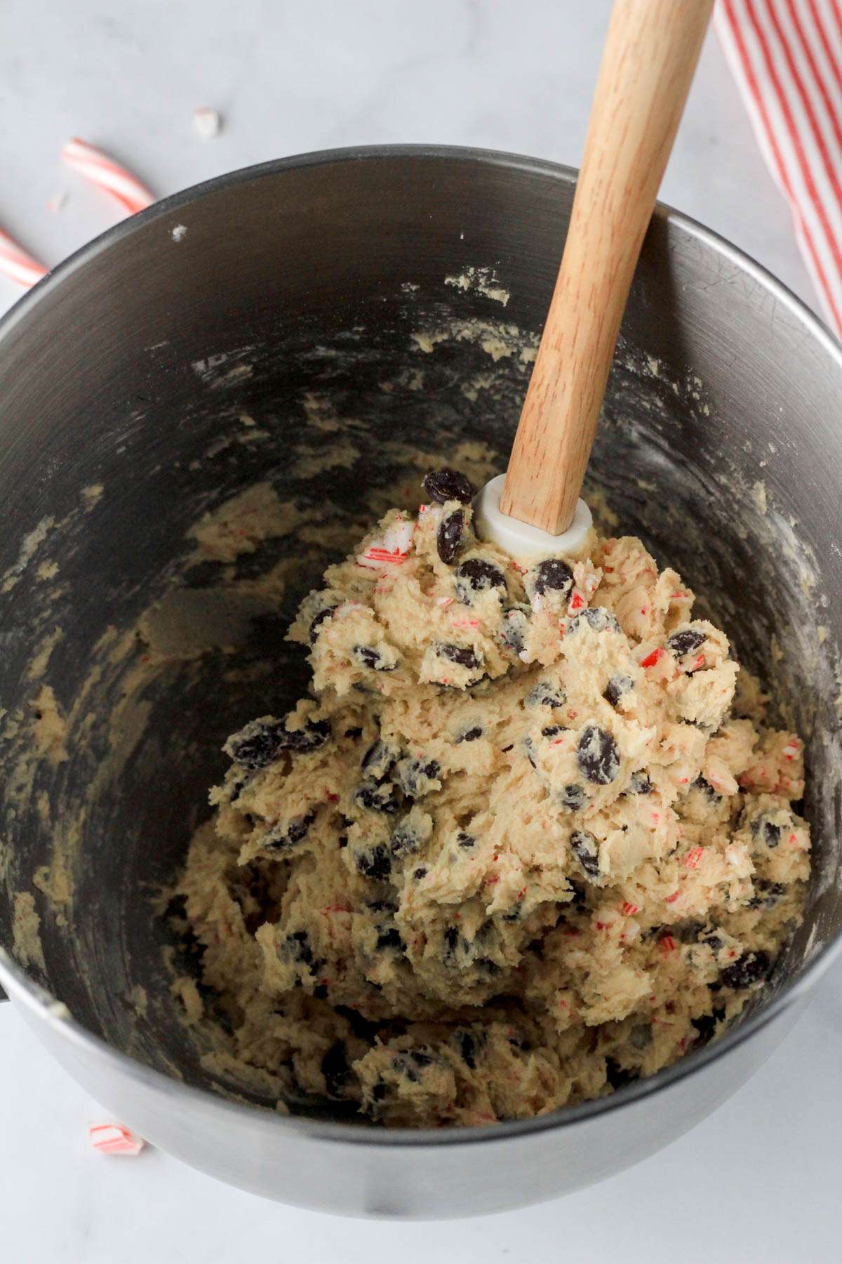 A spatula in a silver bowl of candy cane chocolate chip cookie dough.