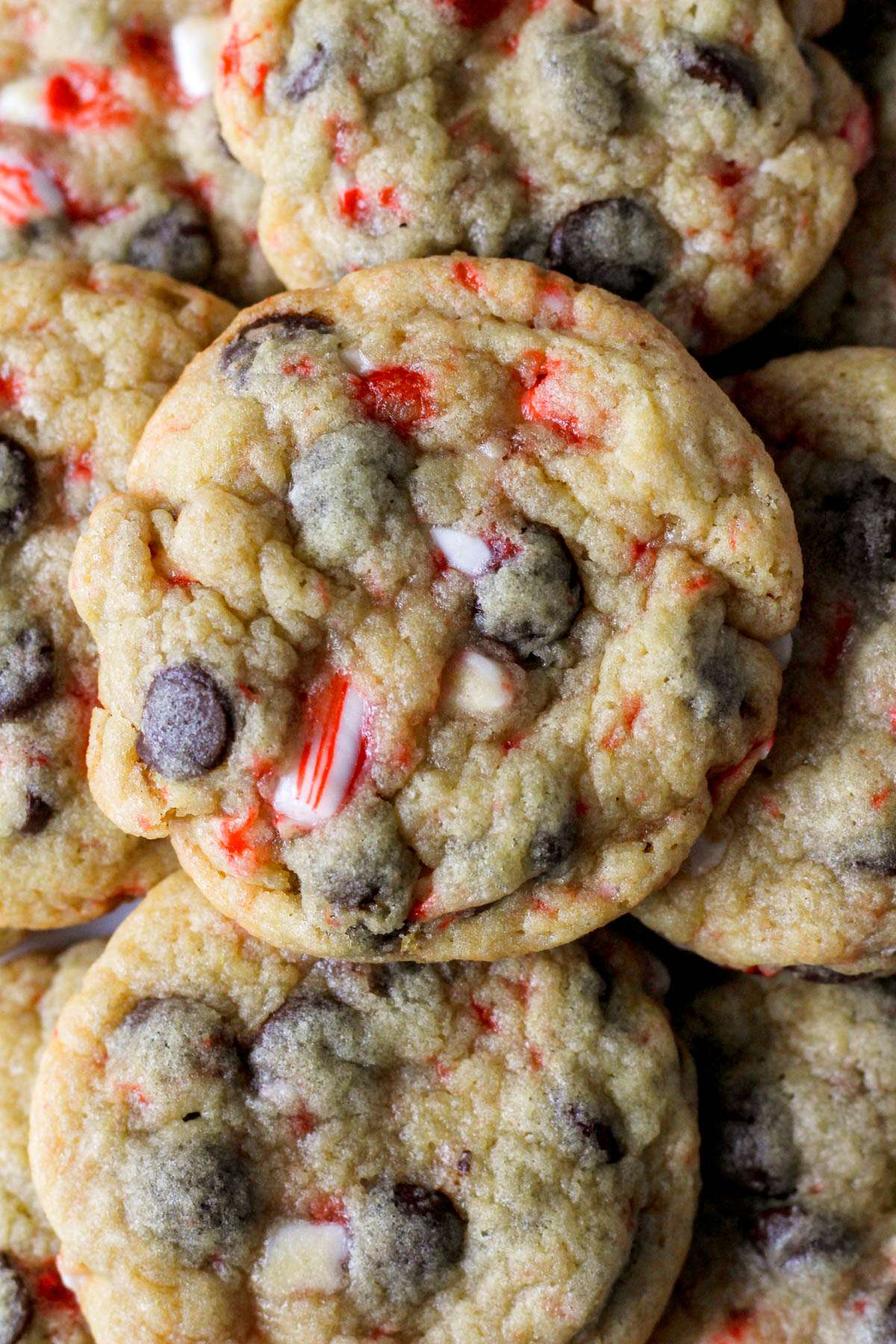 A close up of a peppermint chocolate chip cookie on top of other candy cane studded chocolate chip cookies.