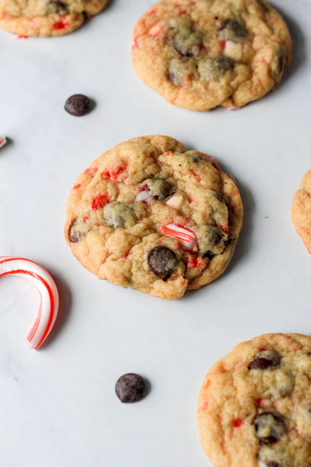 Dairy-free peppermint chocolate chip cookies on a white counter with chocolate chips and candy canes around.