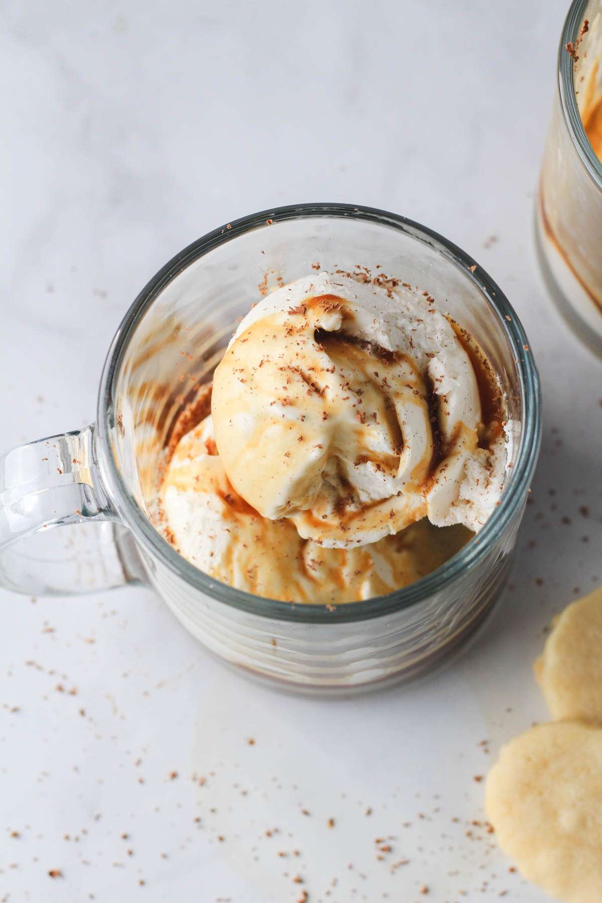 A vegan affogato with vanilla vegan ice cream and a shot of warm espresso in a clear glass mug.