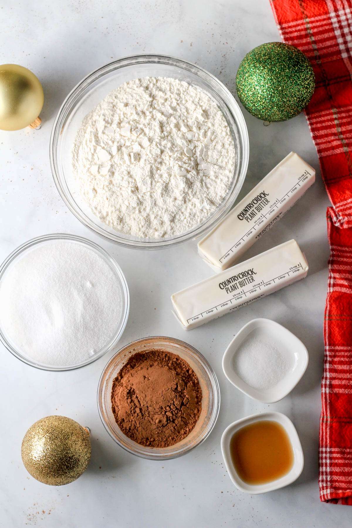Ingredients for vegan chocolate shortbread on a white counter with gold and green christmas balls.