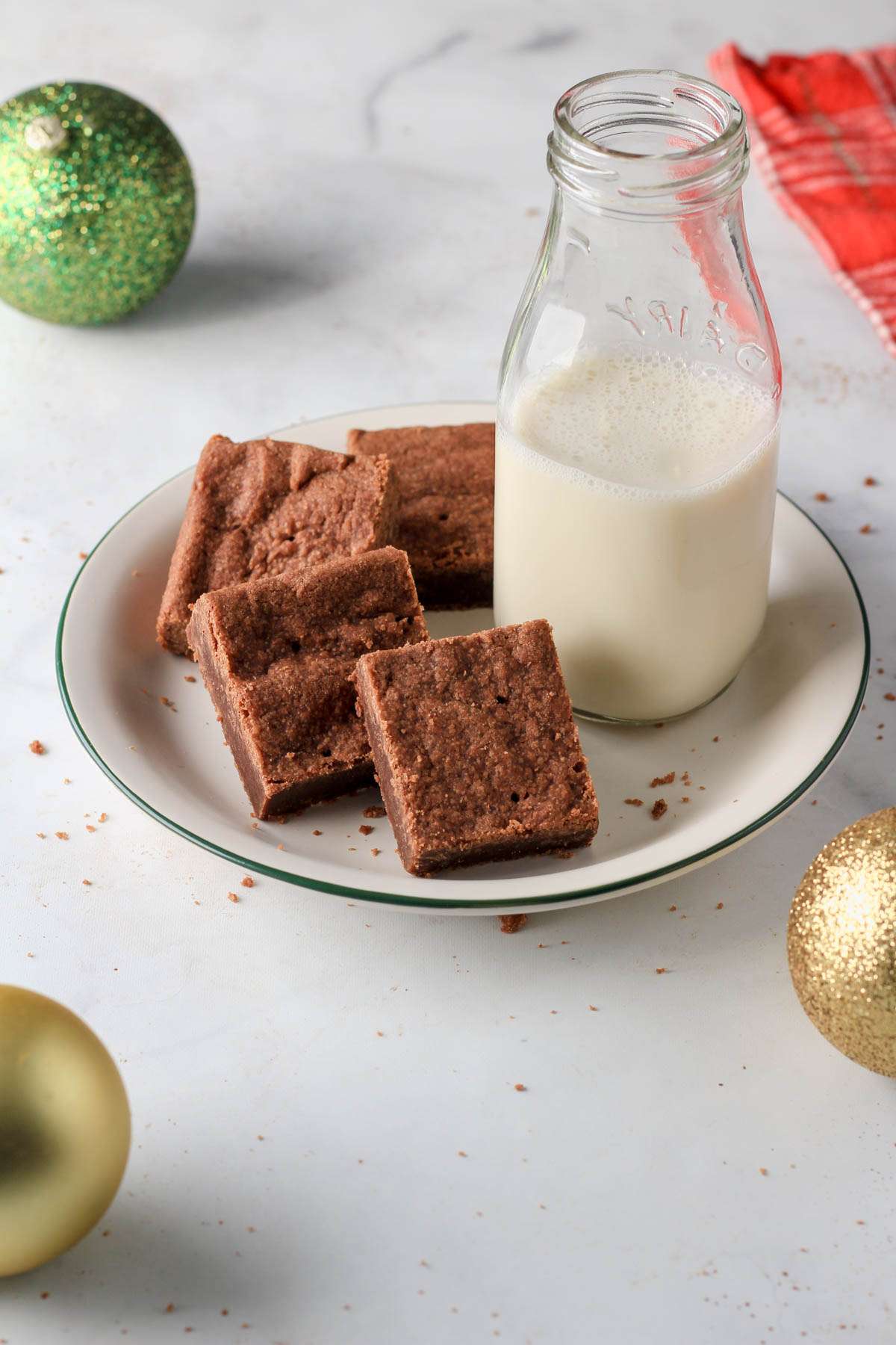 A green and white plate with chocolate shortbread cookies and a glass of non-dairy milk on a white counter.