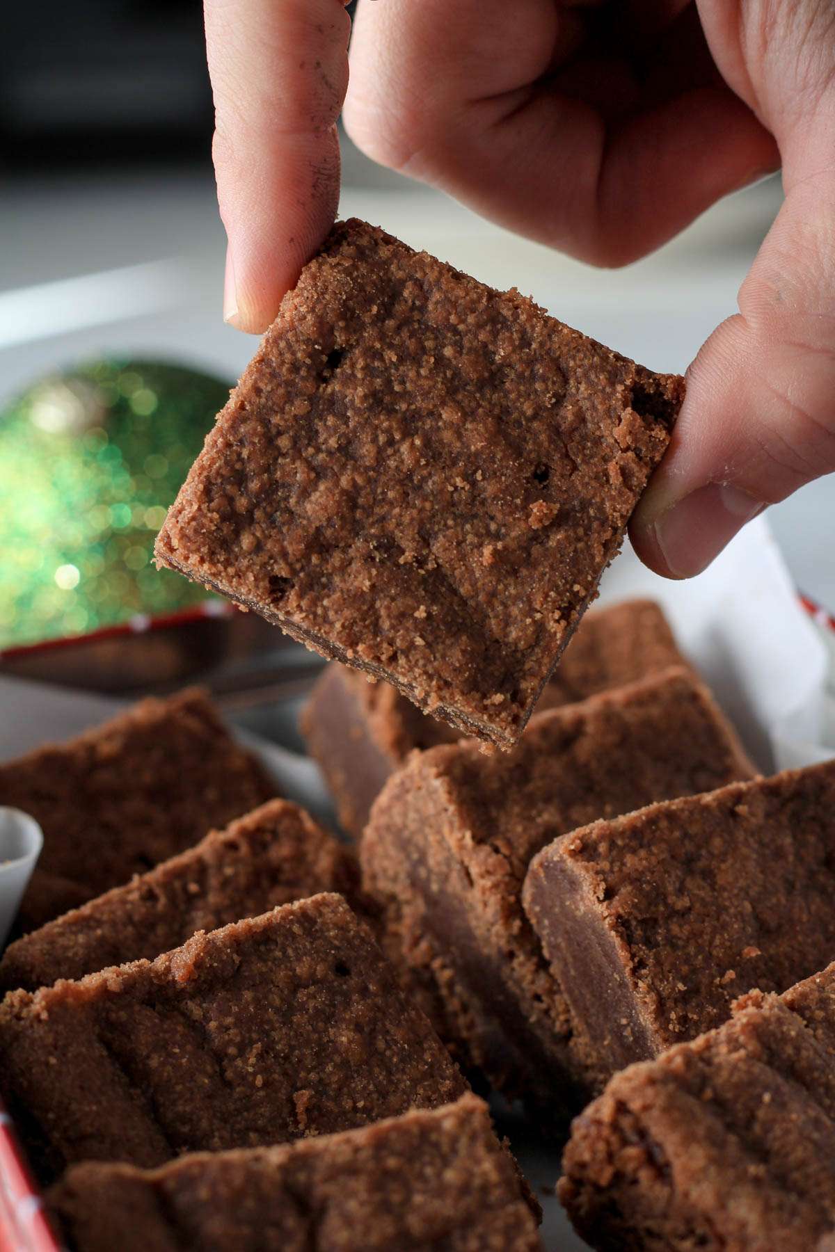 A hand holding a chocolate shortbread bar over a box of chocolate shortbread cookies.