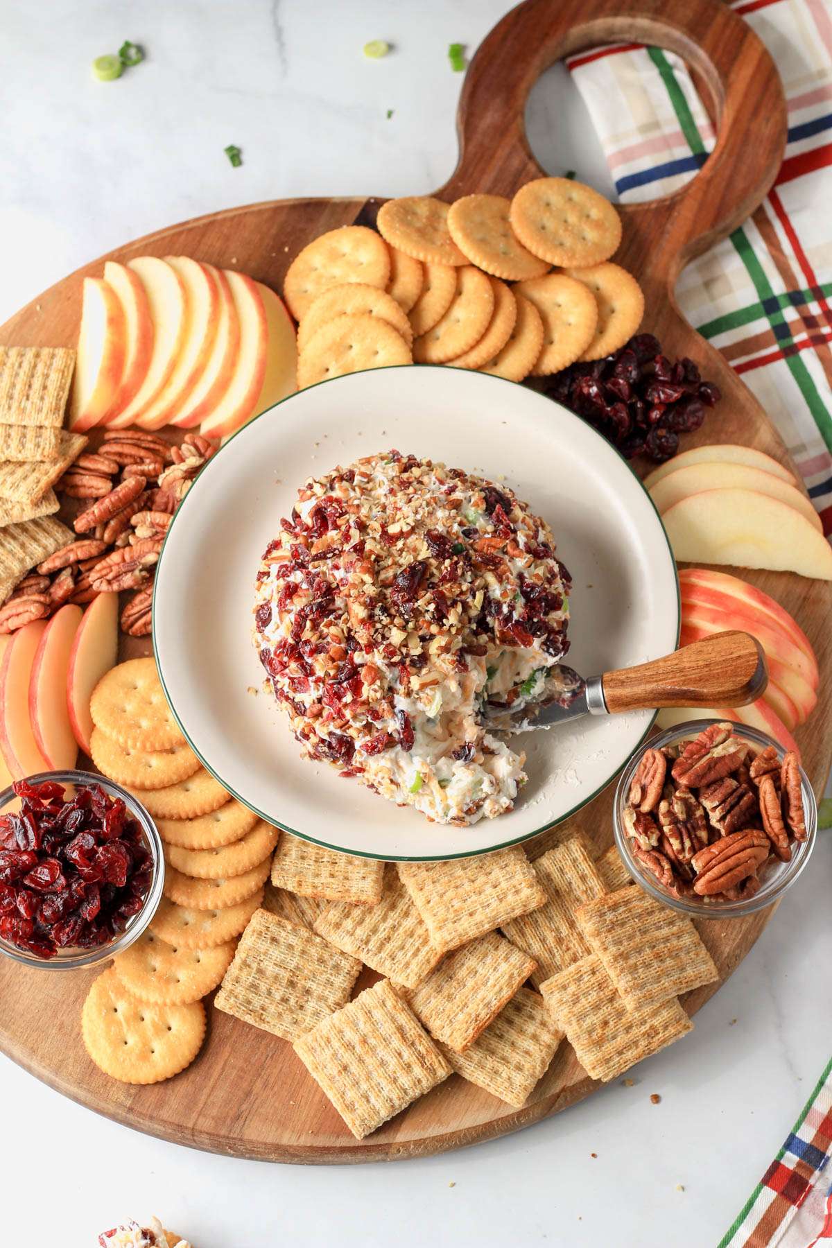 A wooden cheese board filled with crackers, apples, nuts, craisins and a vegan holiday cheese ball in the middle.