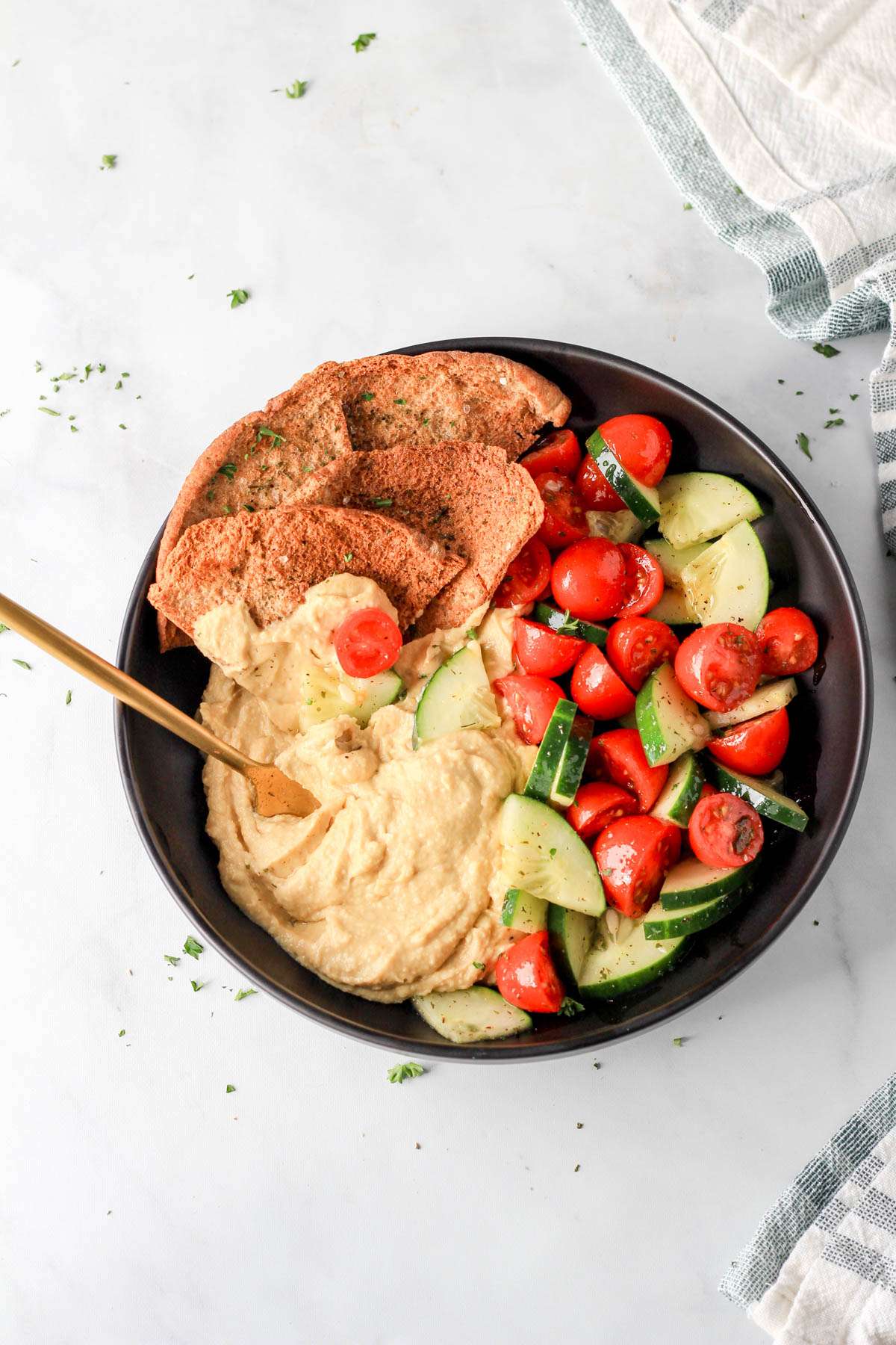 A top down photo of a vegan hummus bowl with a gold spoon on the left side of the bowl.