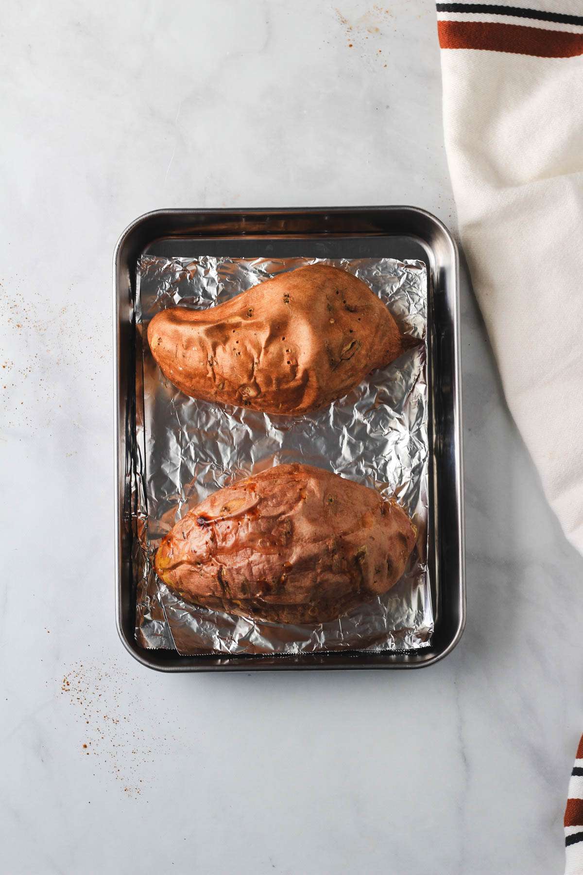 A rimmed baking sheet lined with foil with two sweet potatoes after their first bake.