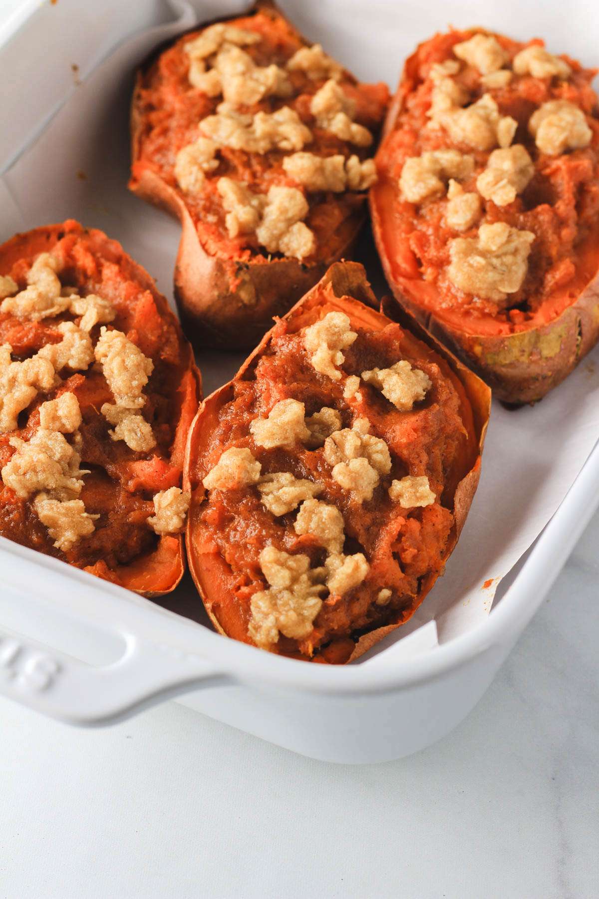 From the side, a vegan twice baked sweet potato in a baking dish with three other dairy-free twice baked sweet potatoes.