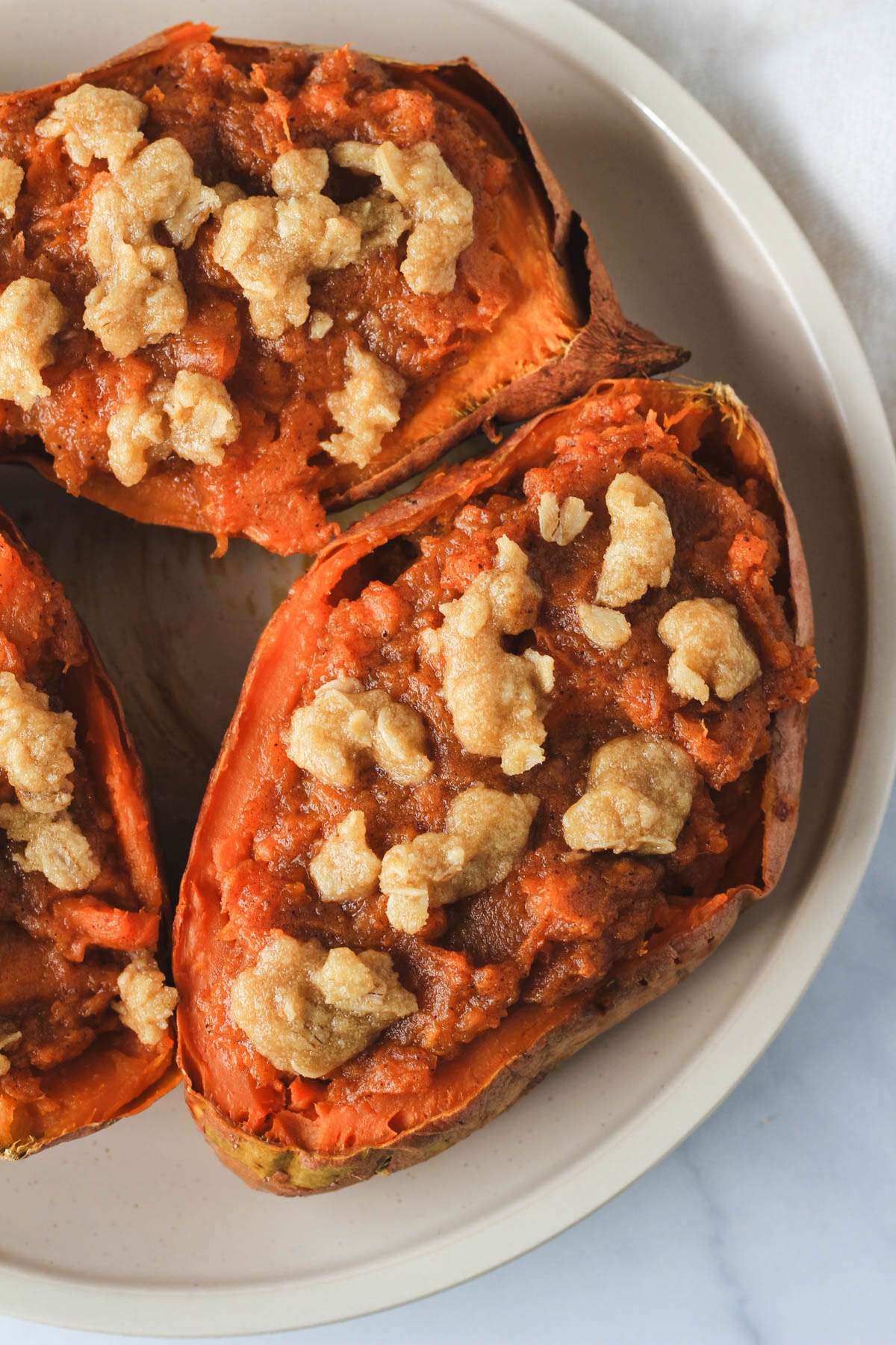 A top down photo of three dairy-free twice baked sweet potatoes on a white plate on a white counter.