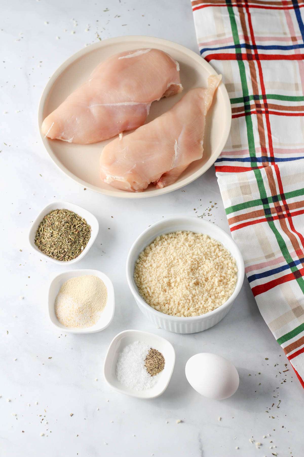 Ingredients for dairy-free air fryer chicken parmesan on a white counter with a dish towel to the right.