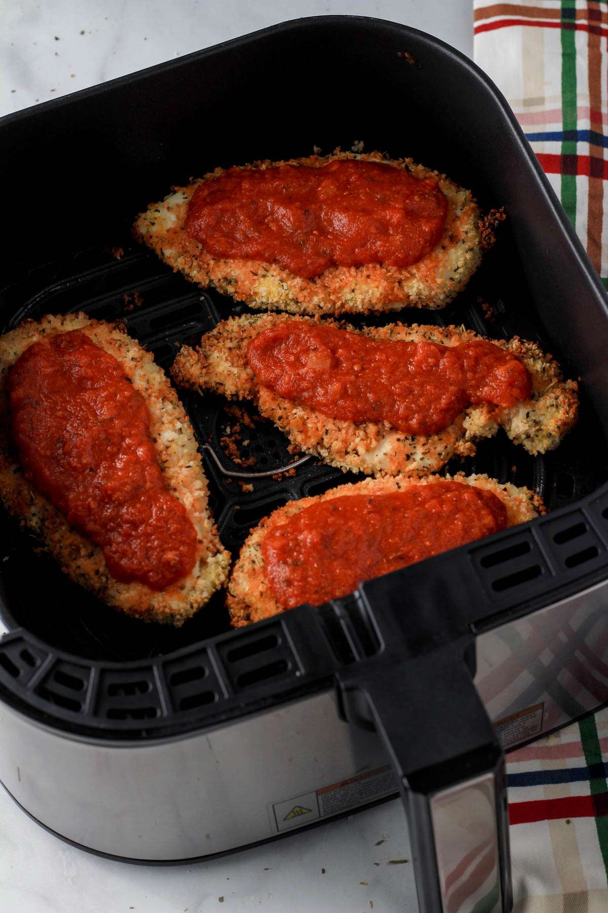 Marinara topped dairy-free chicken parmesan in the air fryer basket.