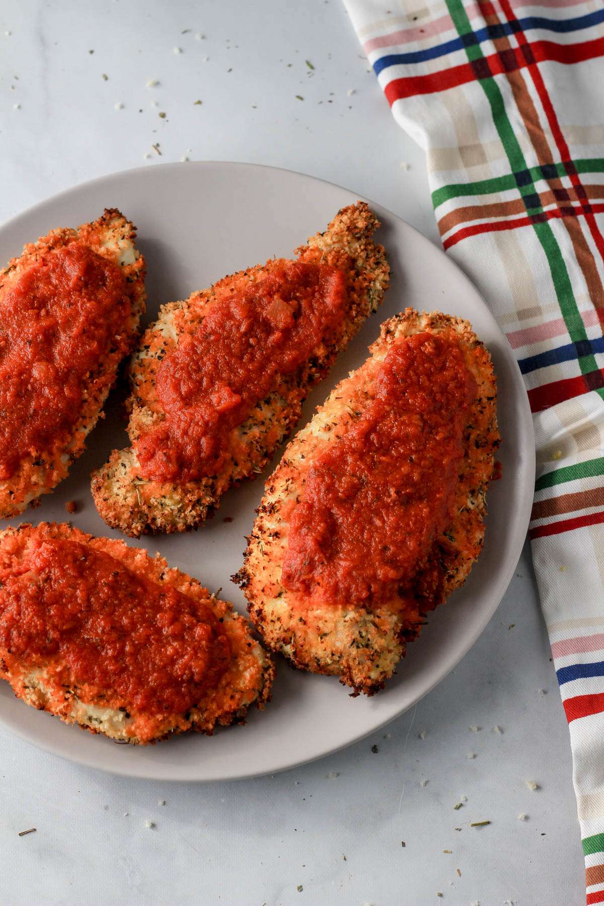 A white plate with four dairy-free air fryer chicken parmesan pieces next to a dish towel.