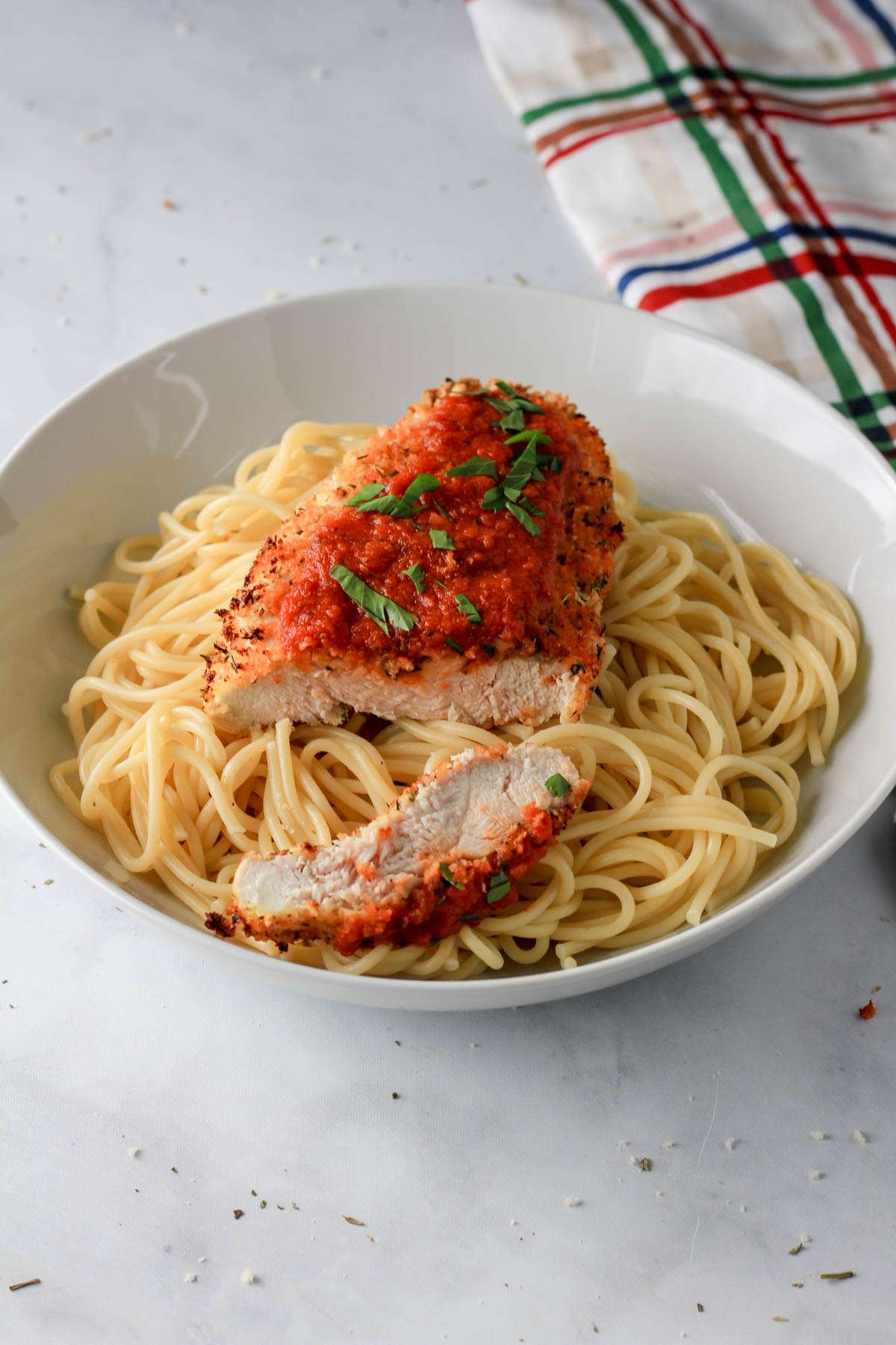 A white bowl with spaghetti topped with a piece of air fryer dairy-free chicken parmesan and chopped parsley.