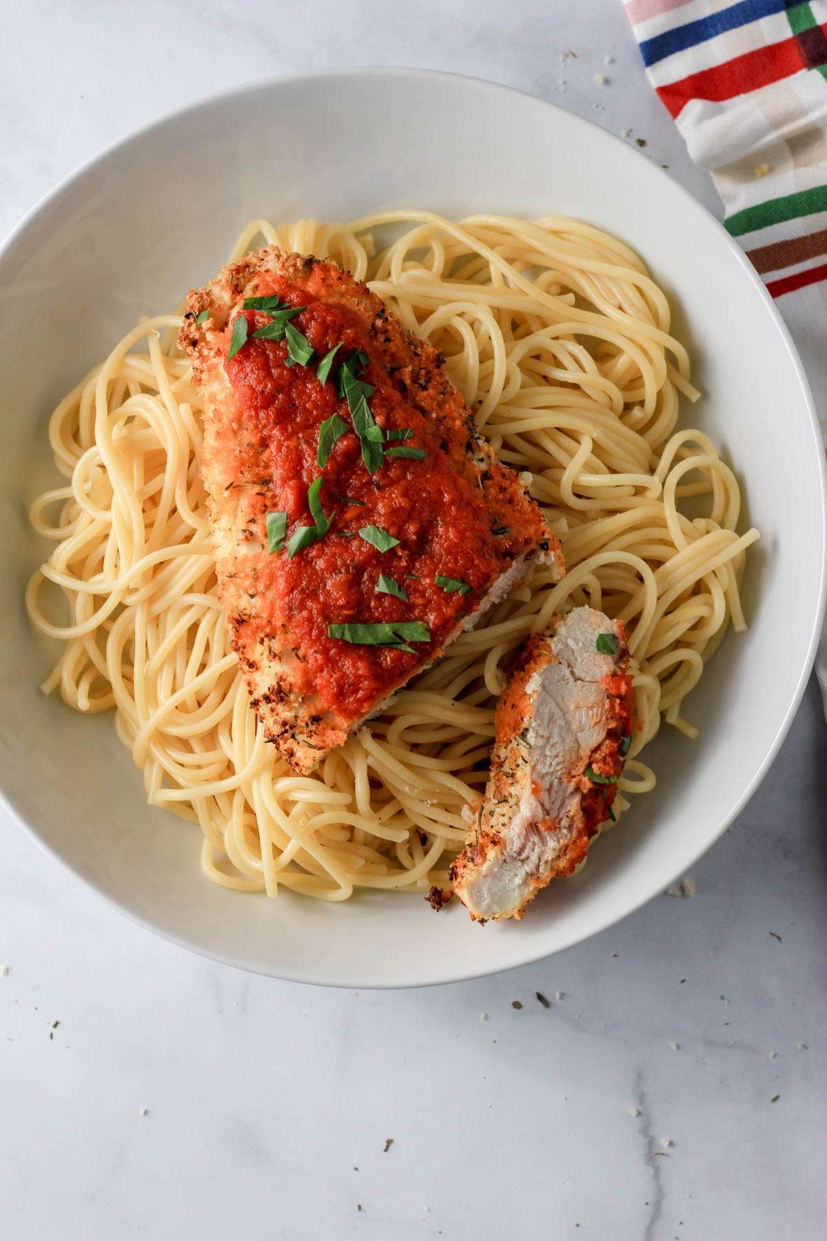 A top down photo of a white bowl with spaghetti topped with dairy-free air fryer chicken parmesan, marinara sauce, and fresh parsley.